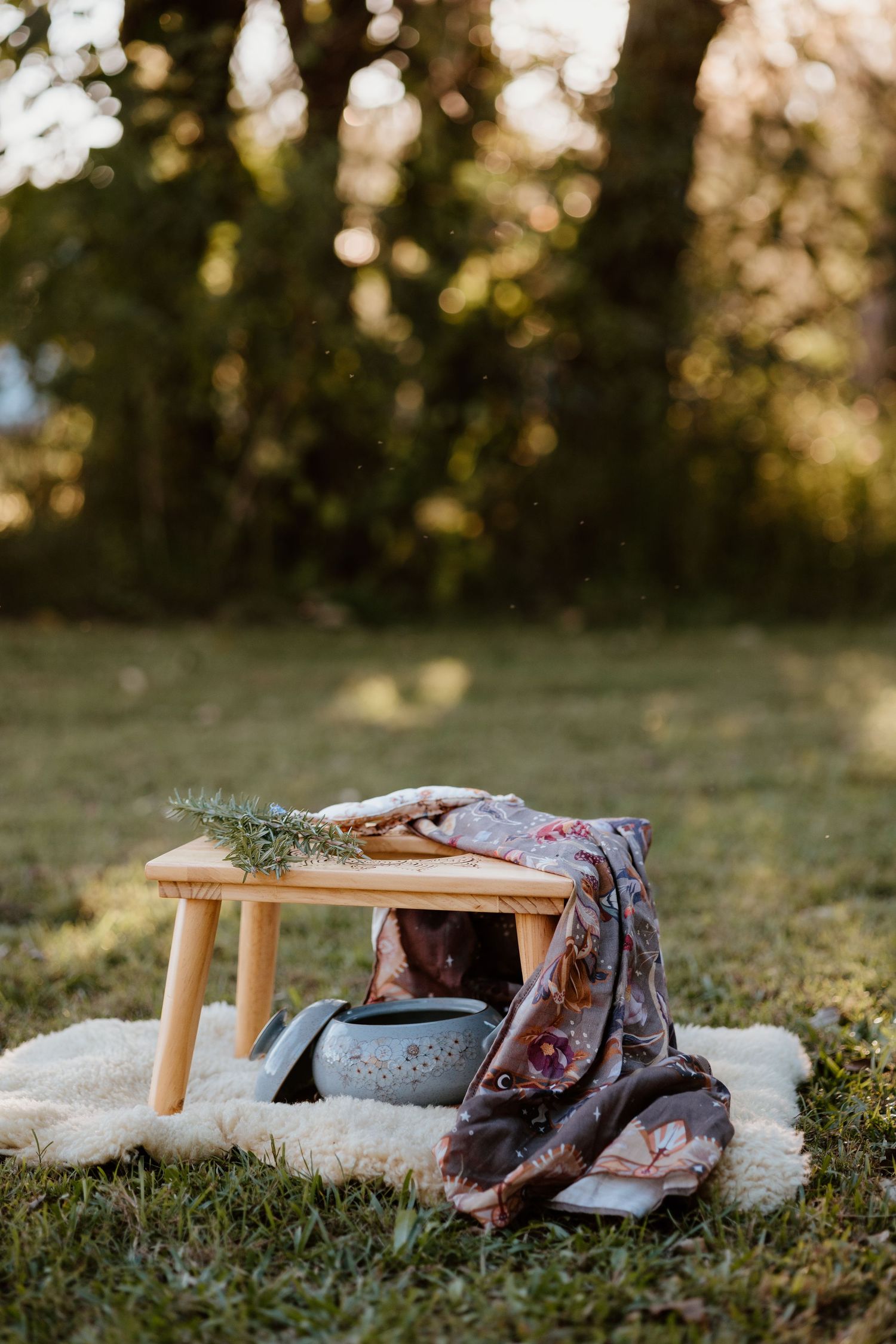 Wooden stool with floral scarf and metal bowl on fluffy rug in sunlit garden setting.