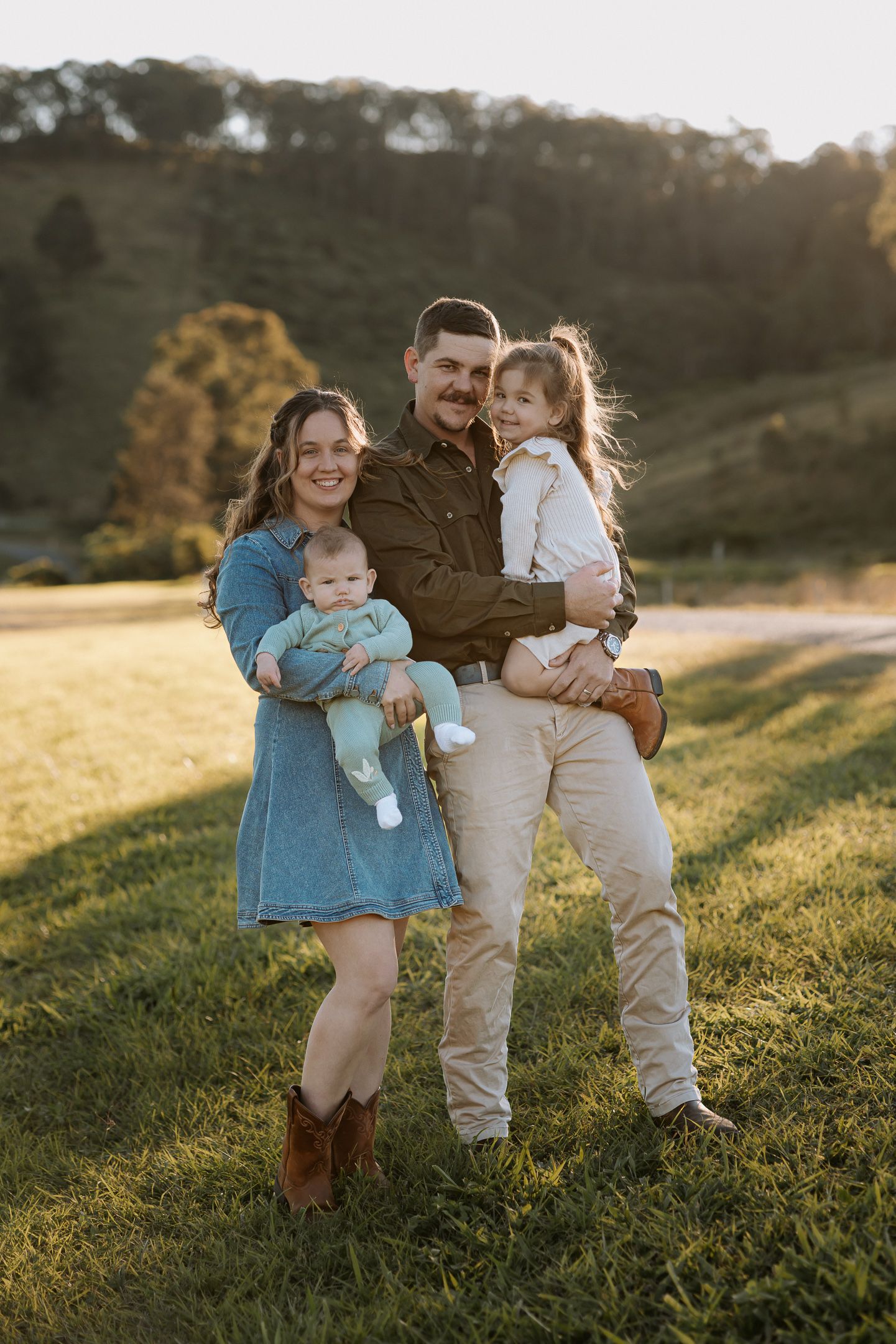 A family shares tender moments together on a grassy hillside during golden hour.