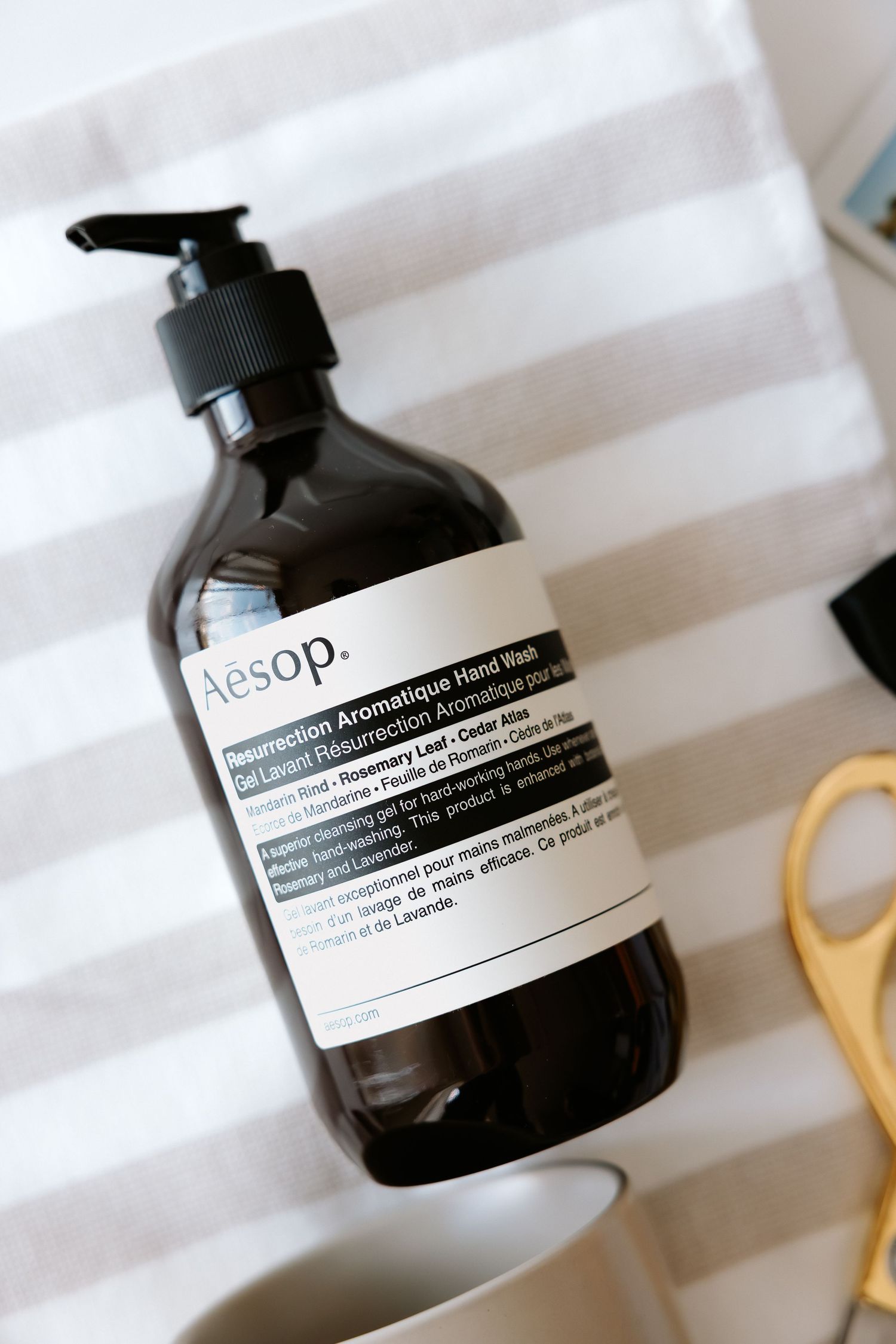 Aesop Resurrection Aromatique Hand Wash pump bottle on striped cloth with gold scissors.