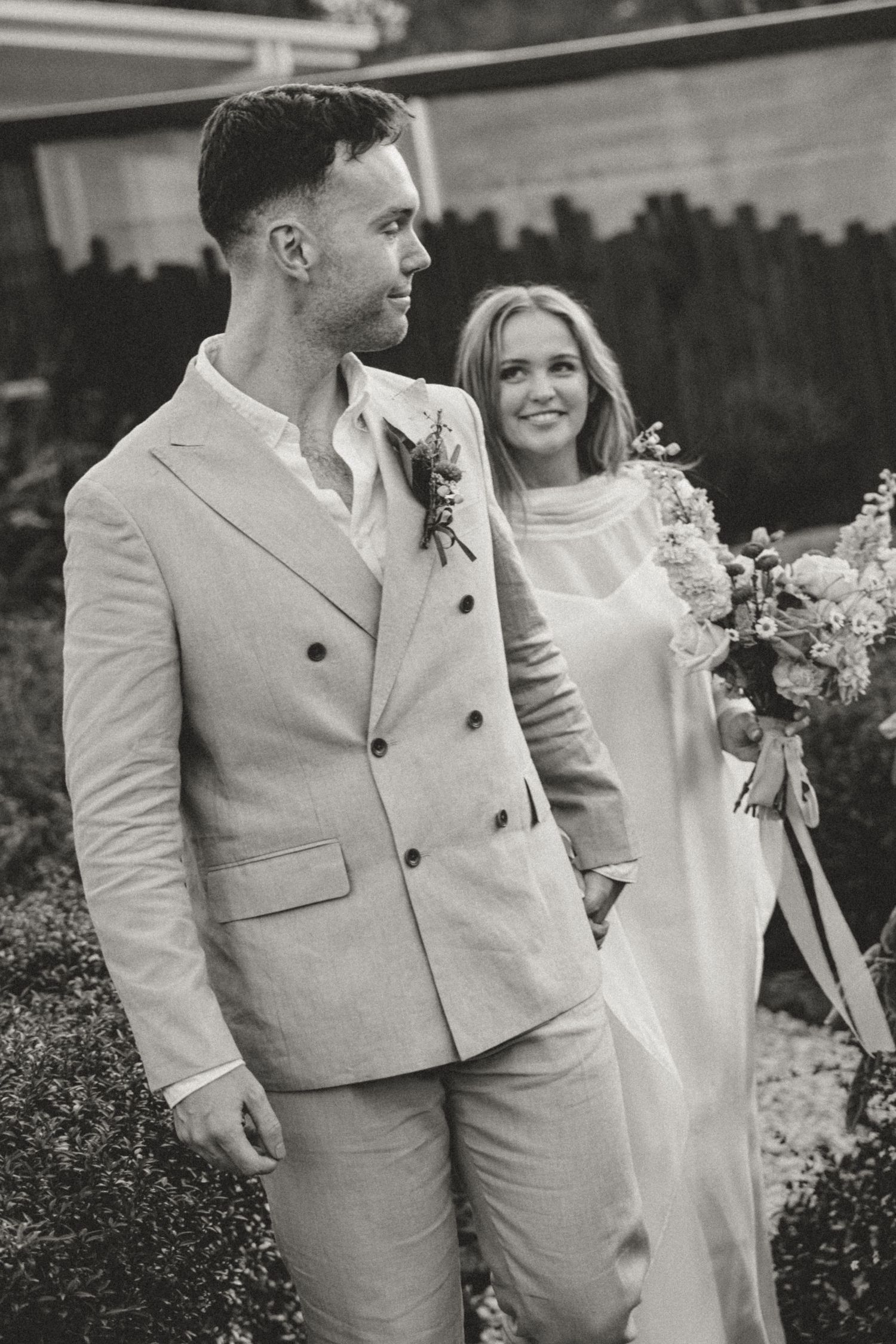 A couple in white and beige attire posing together in a garden setting.