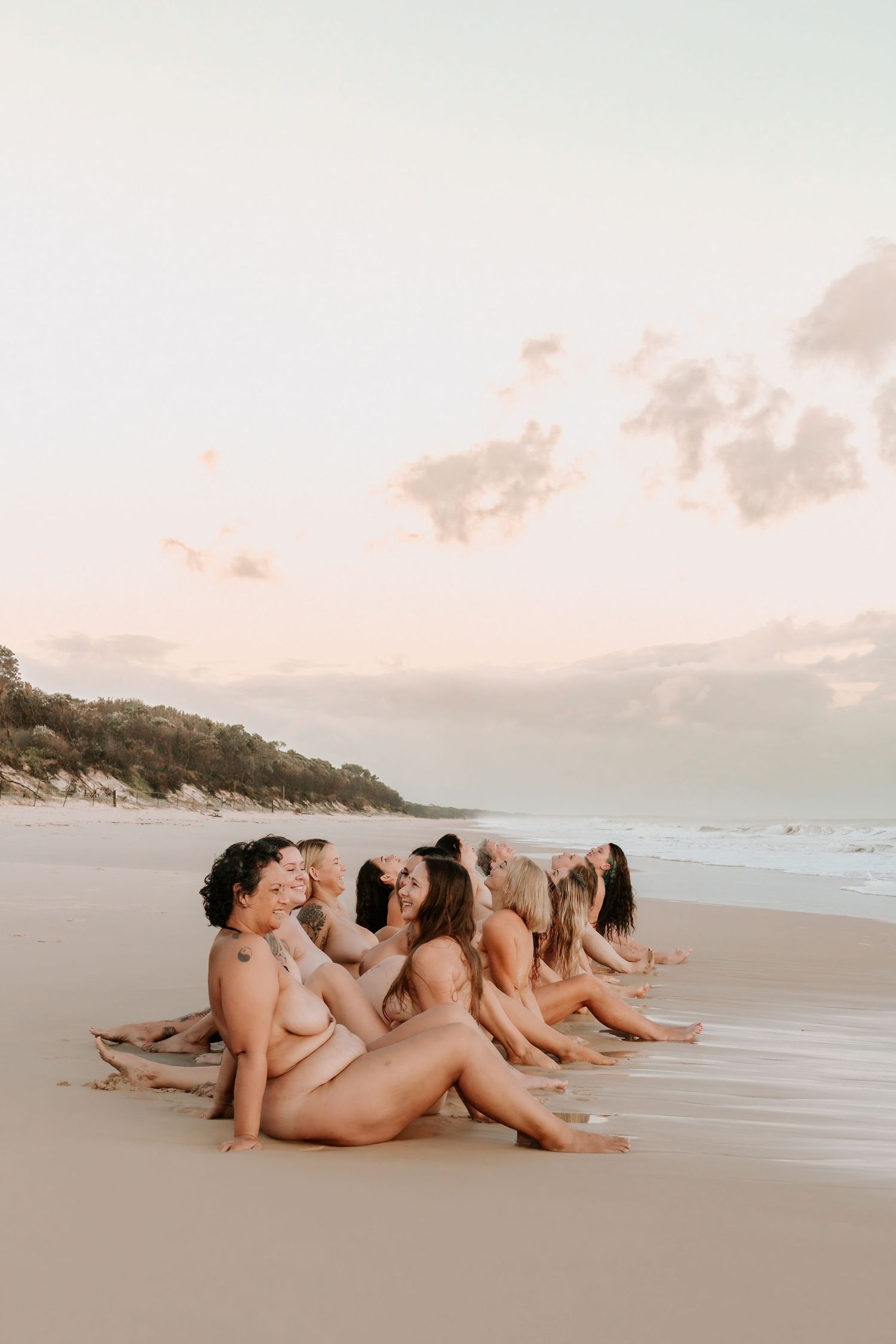 Group of women sitting together on a sandy beach at sunset, enjoying a serene coastal moment.