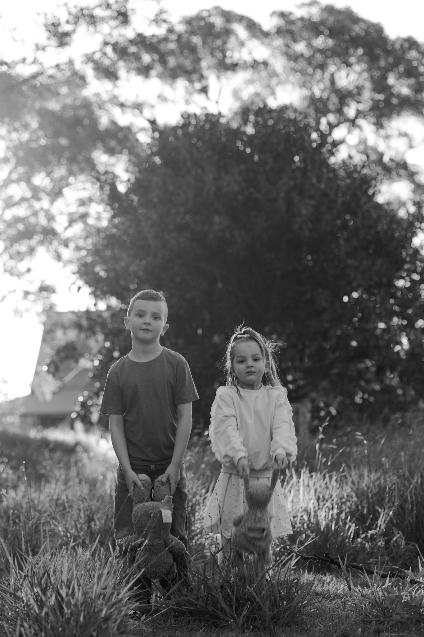 Black and white photo of two young children standing in a grassy field with trees in the background.