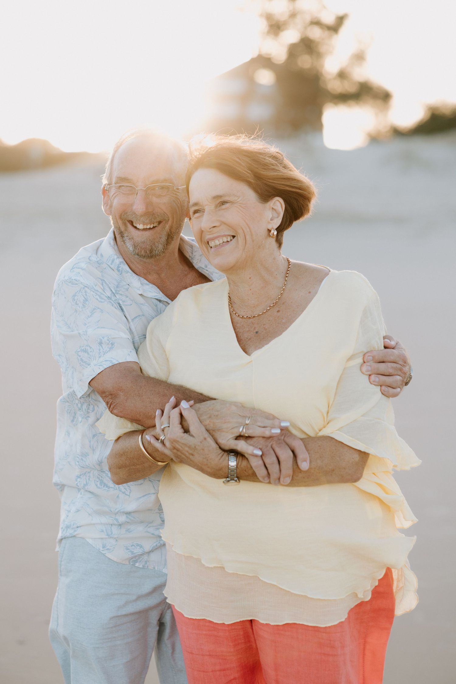 Happy mature couple embracing on a sunny beach, smiling warmly in golden hour light.