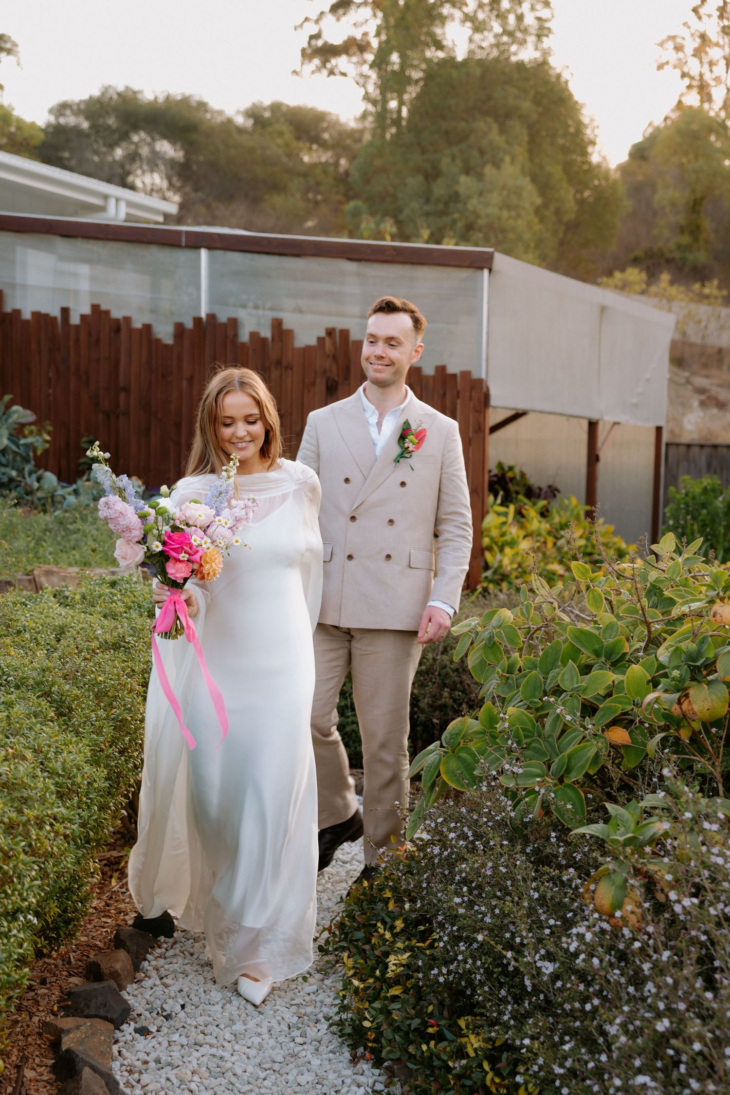 A couple walking along a garden path with colorful flowers and gravel.