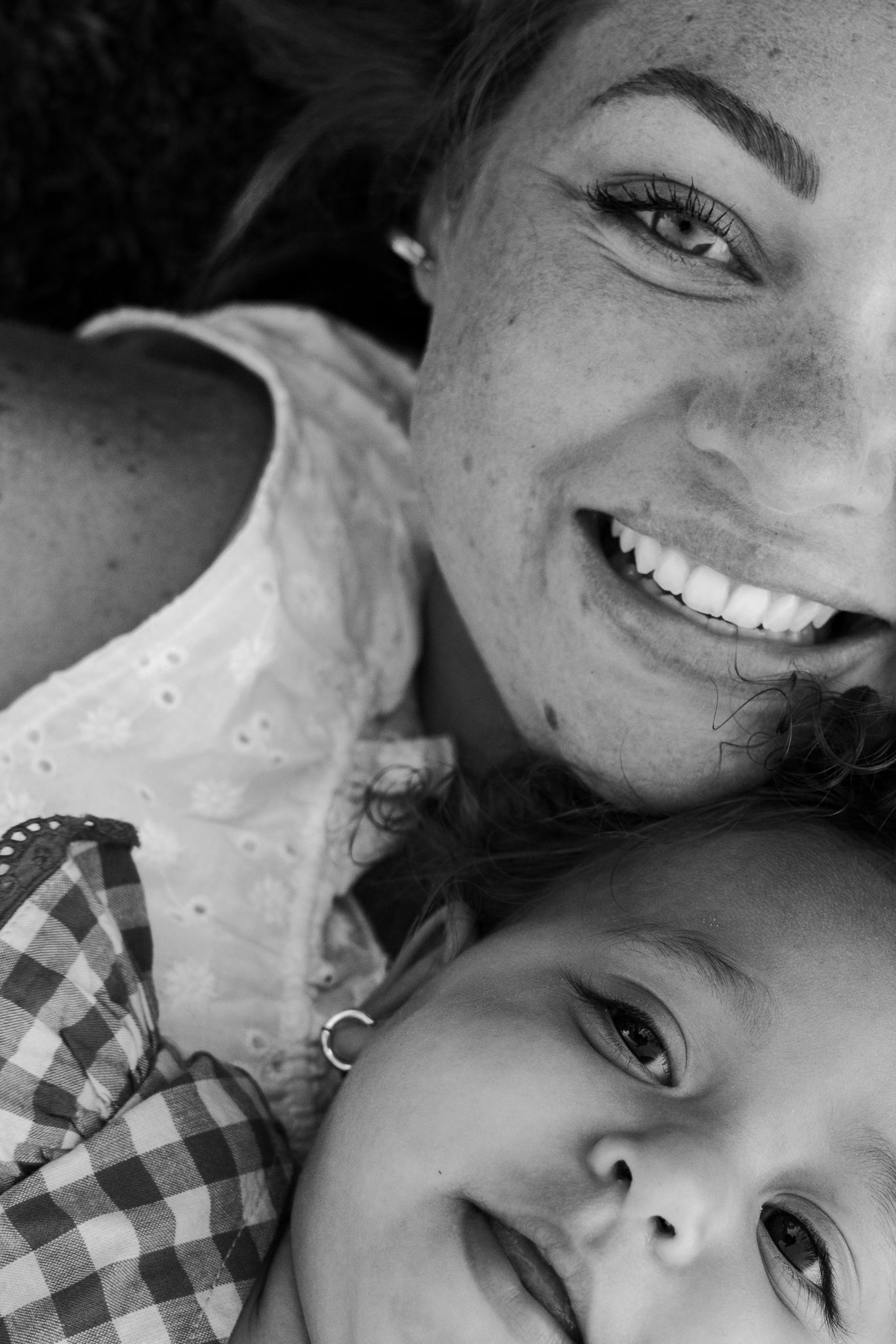 Black and white photo of a smiling woman and young child lying together, sharing a joyful moment.