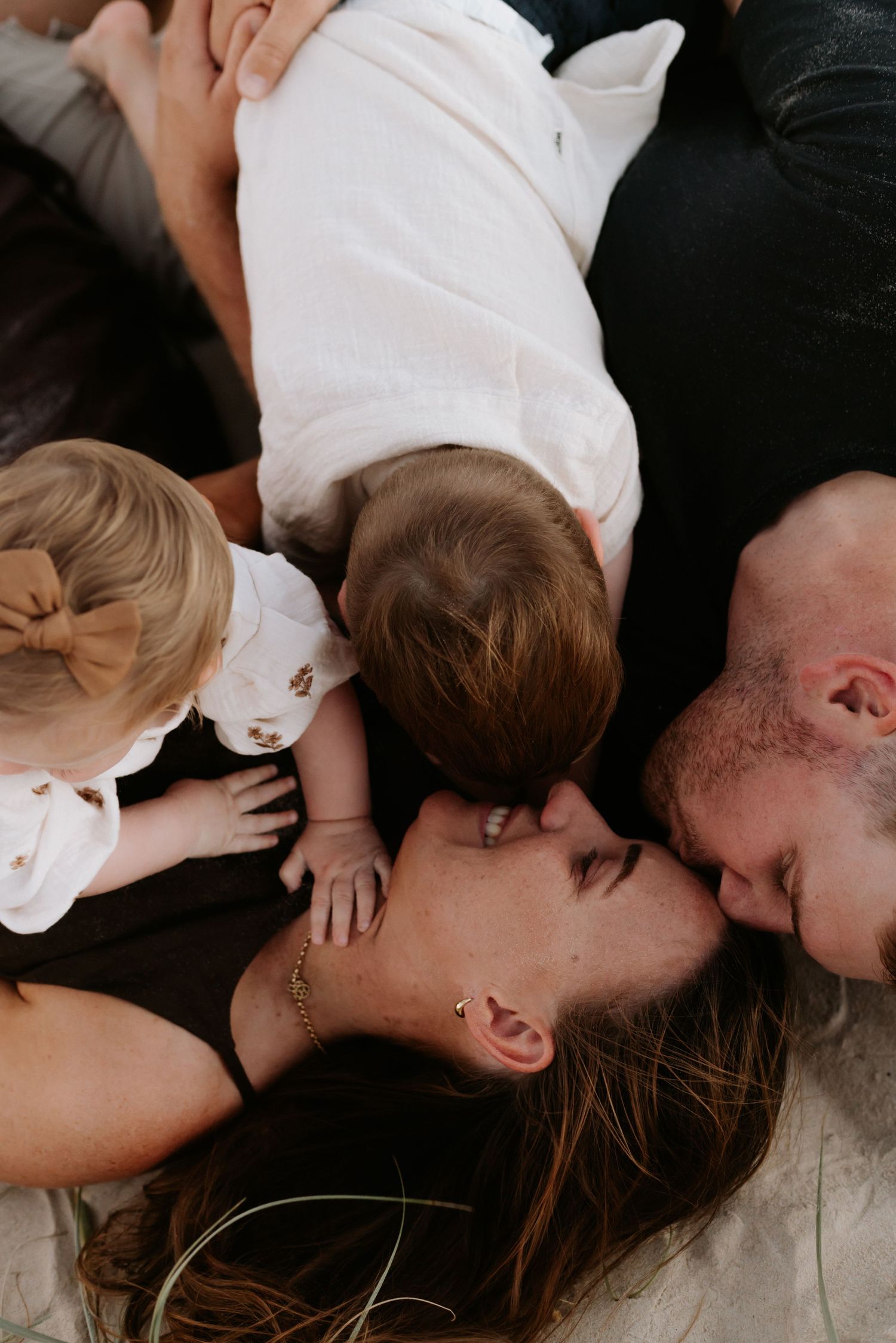 Aerial view of a couple kissing while lying down, surrounded by their two young children in a warm family moment.