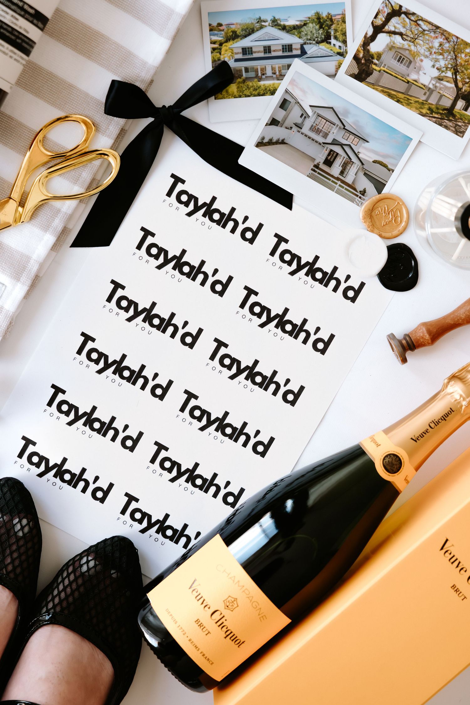 Elegant branding flat lay with Veuve Clicquot champagne, gold scissors, wax seal, and custom Taylahd logo sticker sheet.