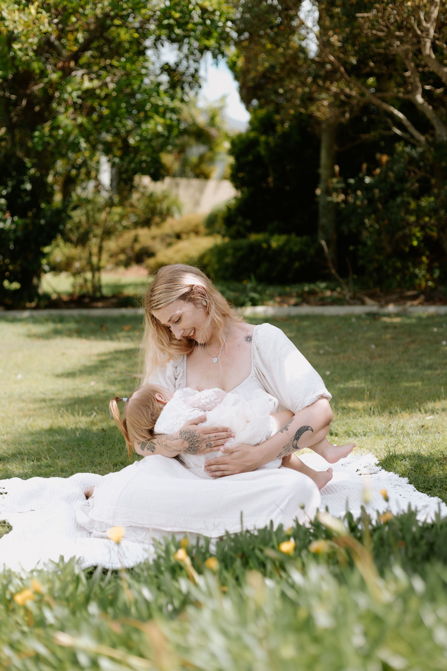 A mother breastfeeding her baby on a white blanket in a sunny green garden.