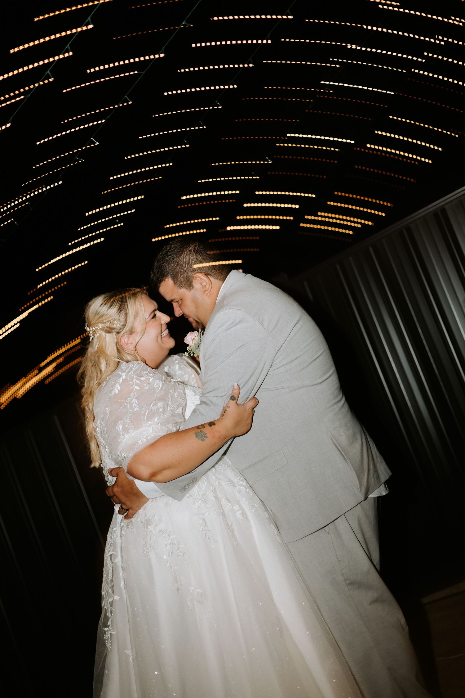 Bride and groom share a romantic moment under glowing arch lights at night wedding reception.