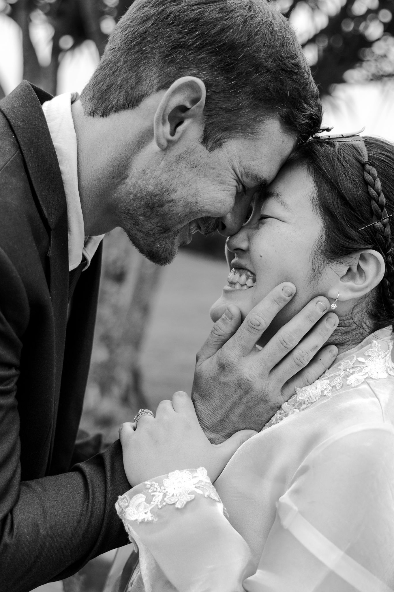 Black and white wedding photo of groom tenderly holding brides face as they share an intimate moment, foreheads touching.