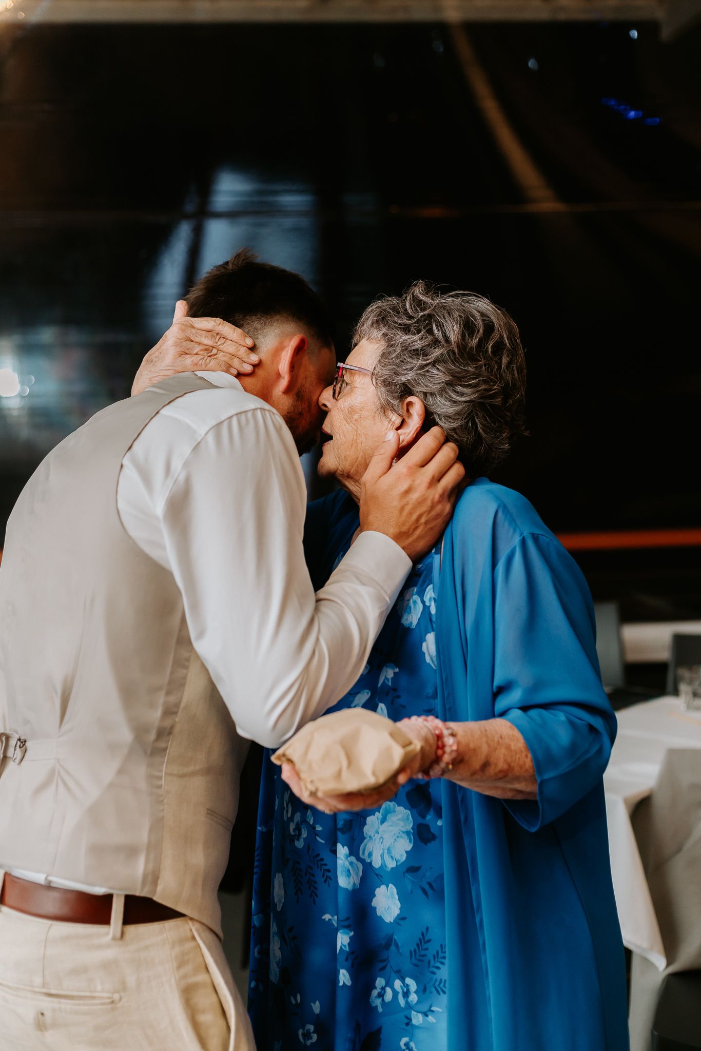 Elderly woman in blue dress tenderly holding grooms face during an emotional wedding dance.