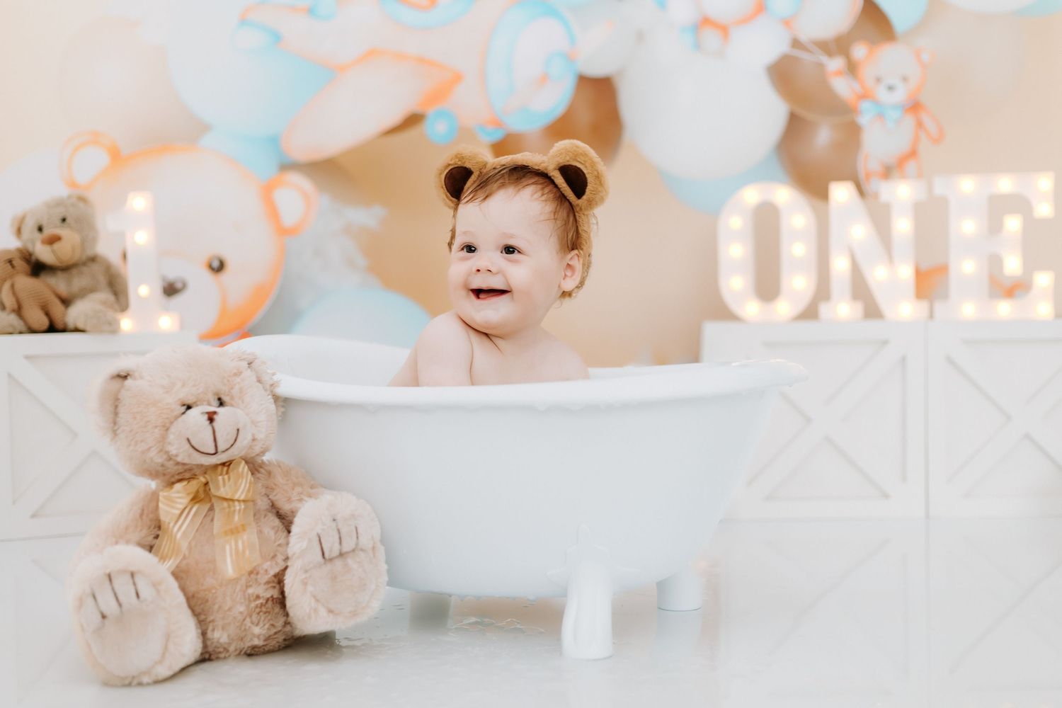 A baby's first birthday celebration with teddy bears, balloons, and cake decorations in soft pastel colors.