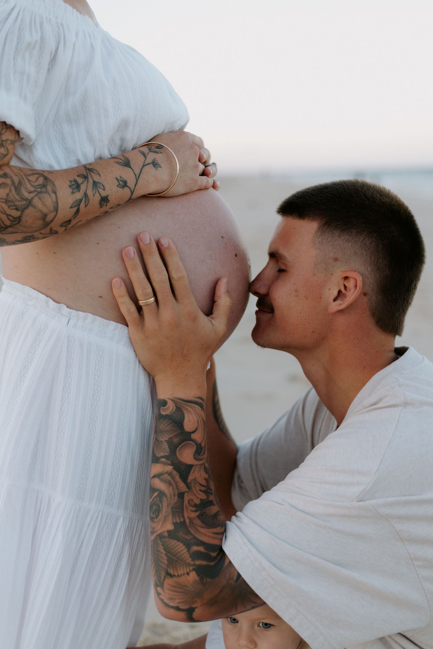 A series of photos showing someone in white kissing a pregnant belly with visible tattoos against a light background.