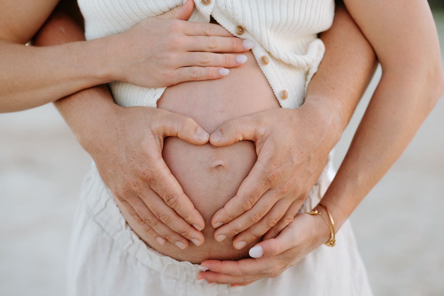 Couple forming a heart shape with hands on pregnant belly, maternity photo capturing love and pregnancy.