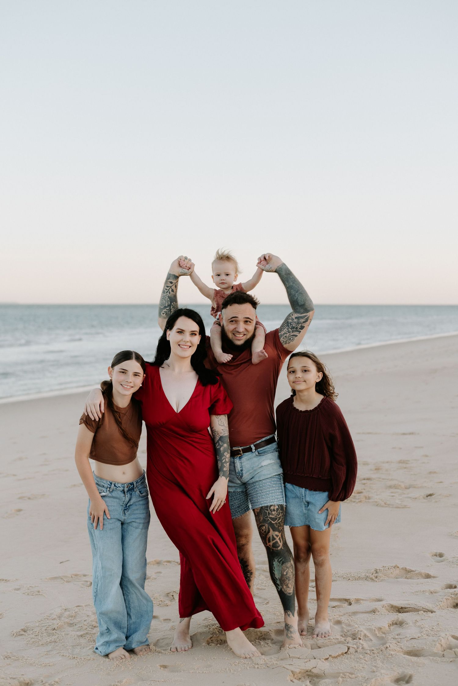 A group of friends laughing and posing together on a sandy beach at sunset.