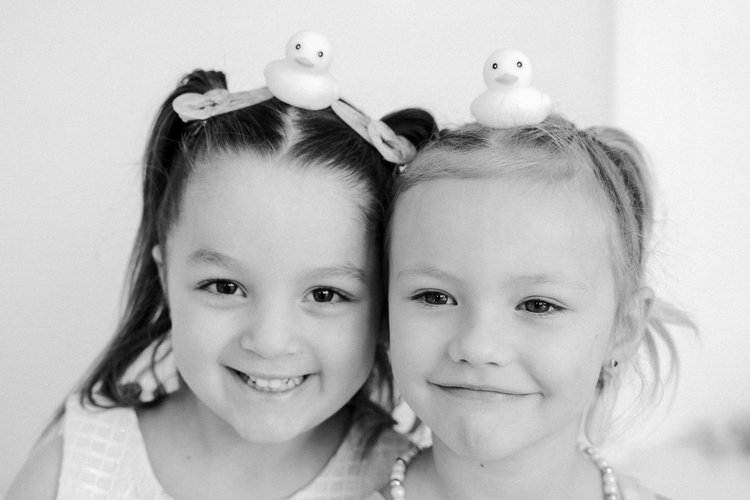 Two smiling girls with rubber duck hair clips pose together in a charming black and white portrait photo.