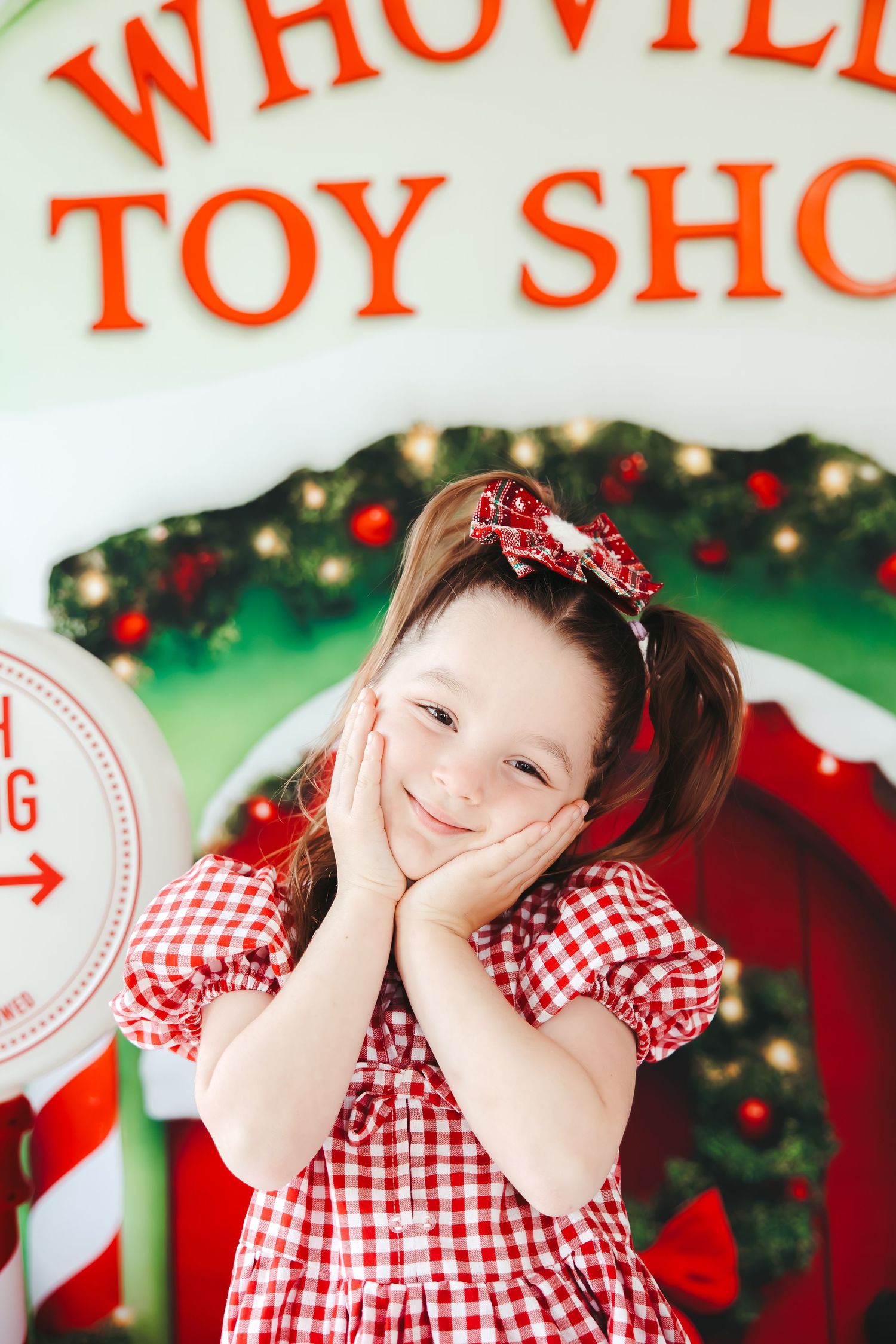Young girl in red gingham dress poses cheerfully in front of Whoville Toy Shop Christmas display.