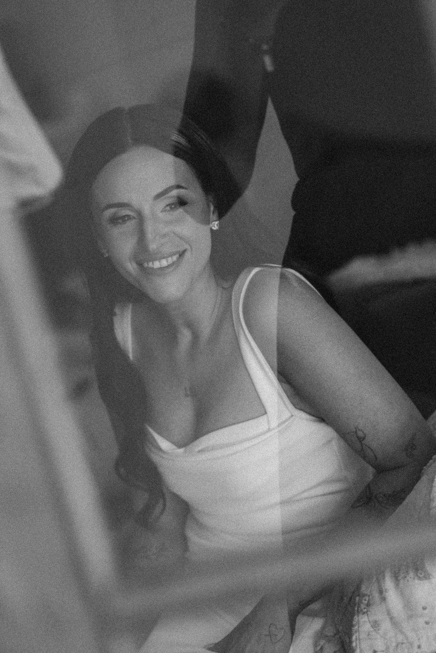 A black and white portrait shows someone in a white tank top with a bright smile against a dark background.