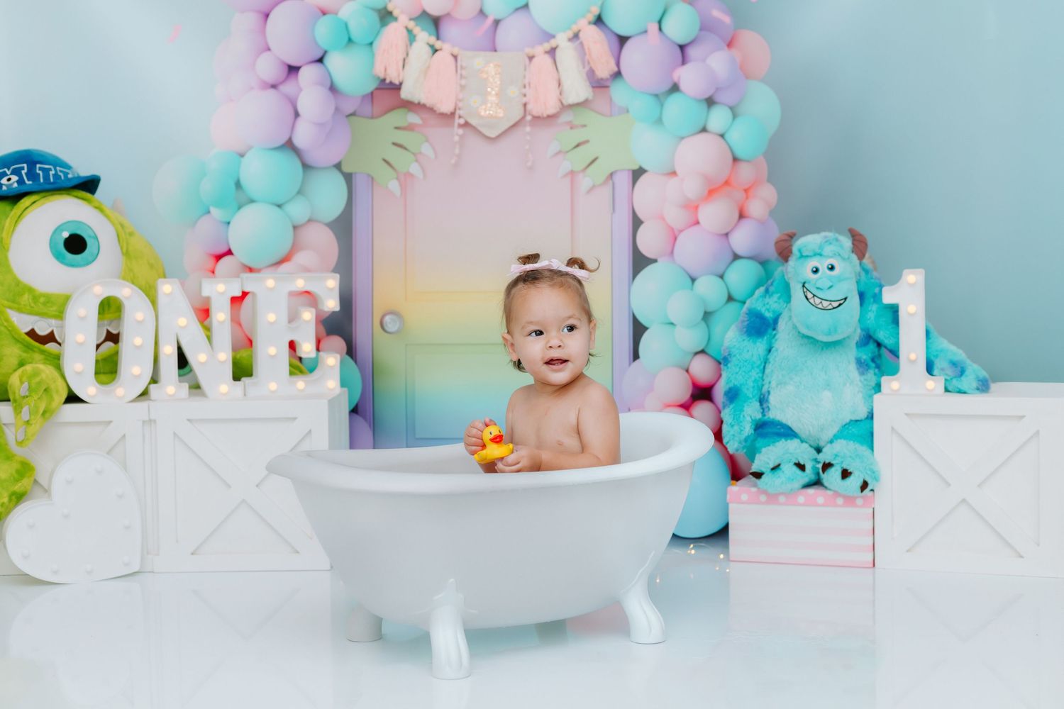 Pastel balloon arch with pink and blue colors decorates a cake smash photo setup with Monsters Inc theme decor.