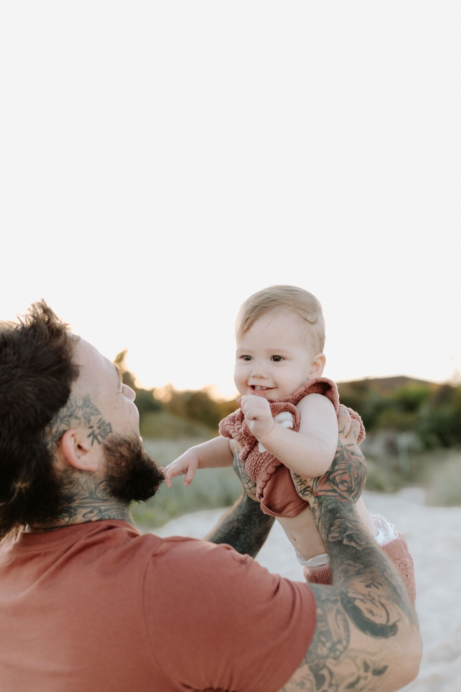 Parent and baby share joyful moments playing together on a sandy beach at sunset.