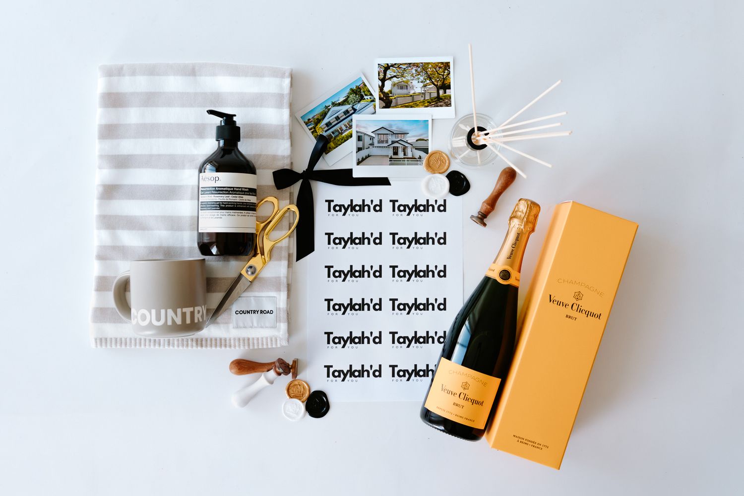 Luxury gift set with Veuve Clicquot champagne, Aesop hand wash, striped towel, and curated accessories on white background.