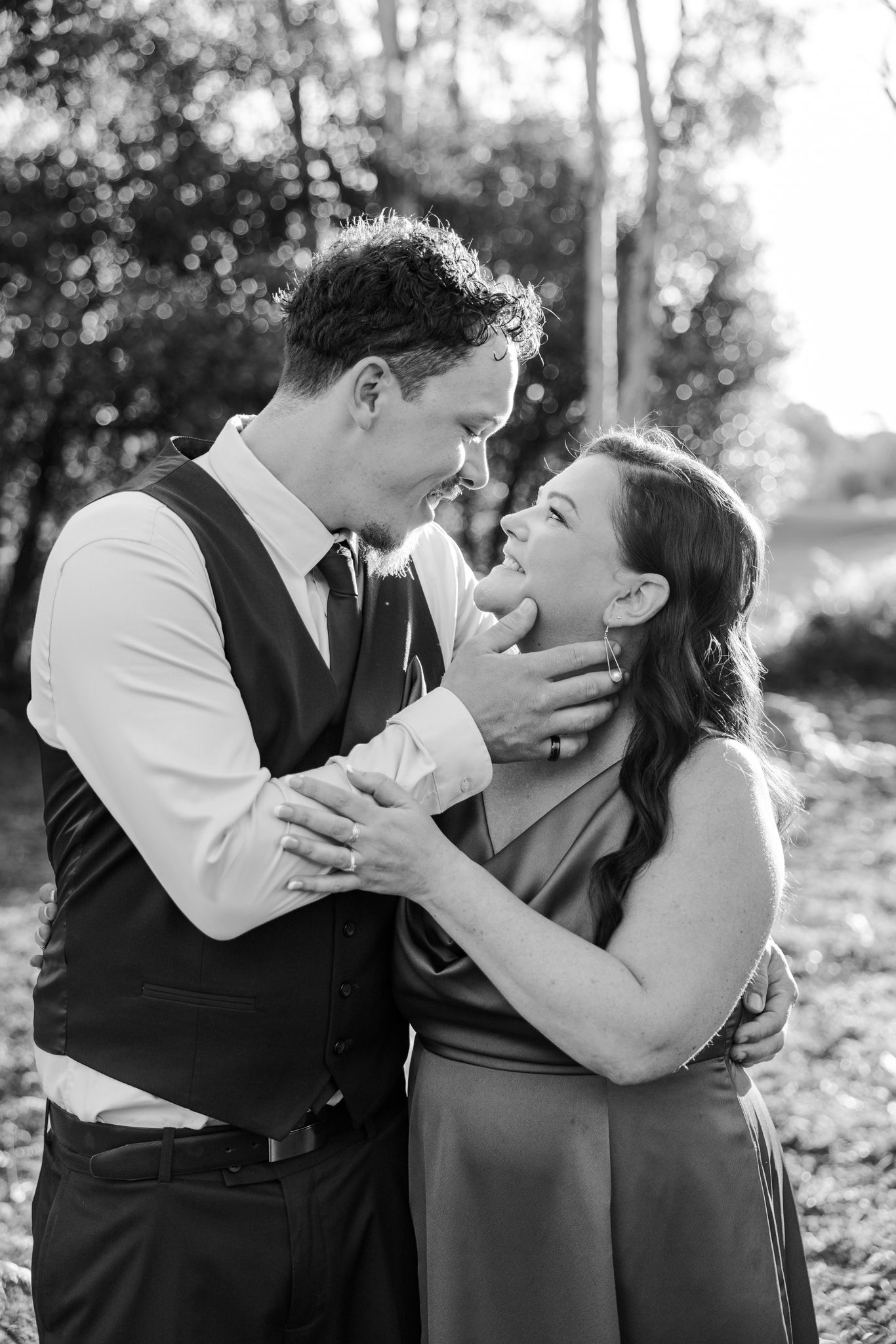 Black and white photo of a couple in formal attire gazing at each other tenderly outdoors.