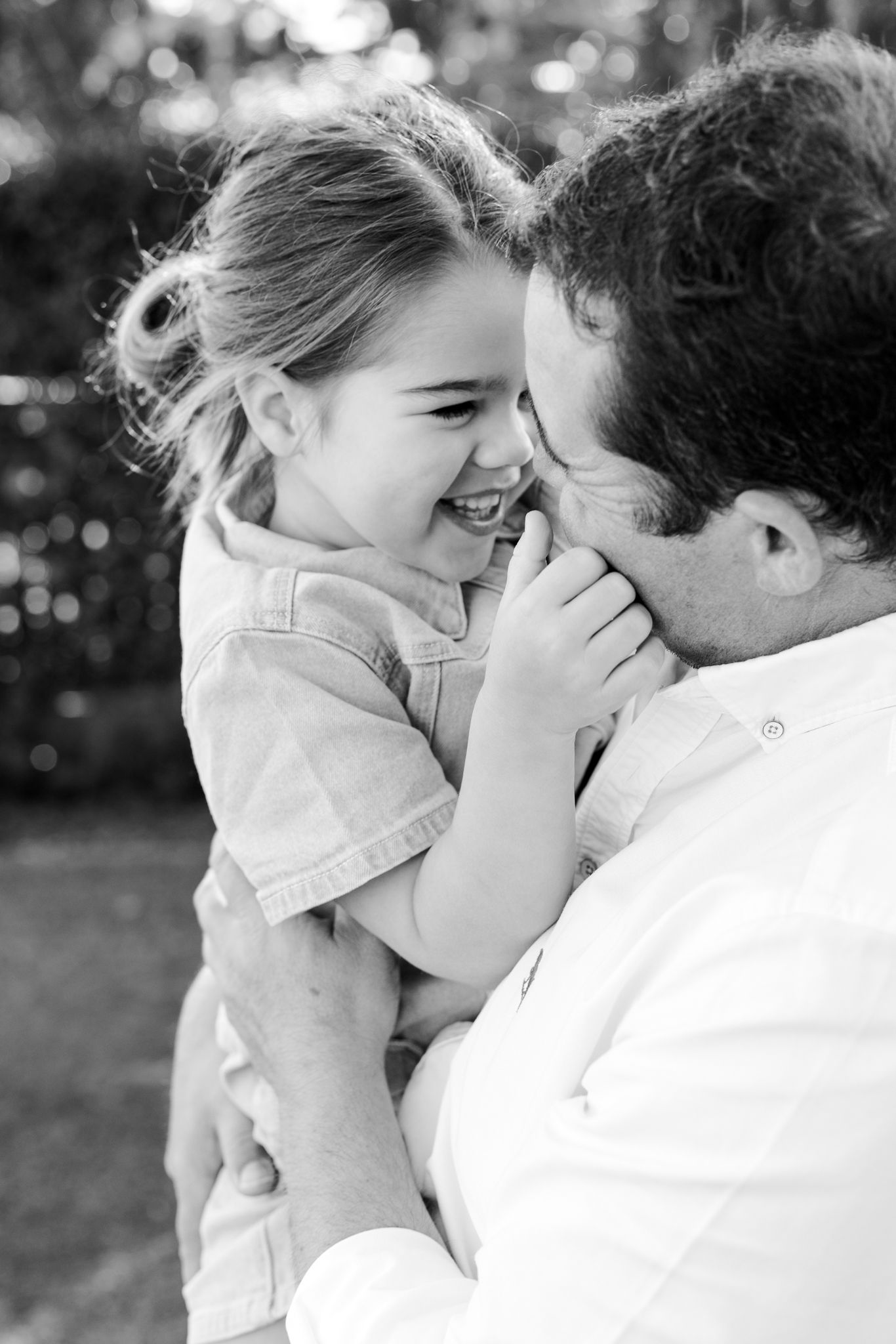 Black and white photo of a laughing child being held by a man, sharing a joyful moment outdoors.