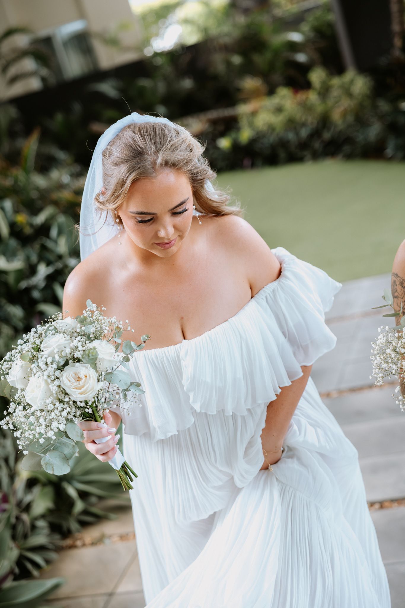 Bride in off-shoulder white pleated gown holding bouquet of white roses and baby's breath.