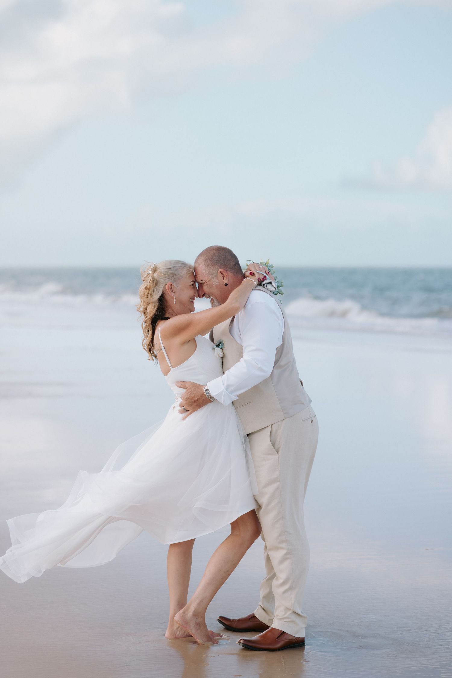 A romantic beach wedding photo series showing a couple in white embracing and dipping against an ocean backdrop.