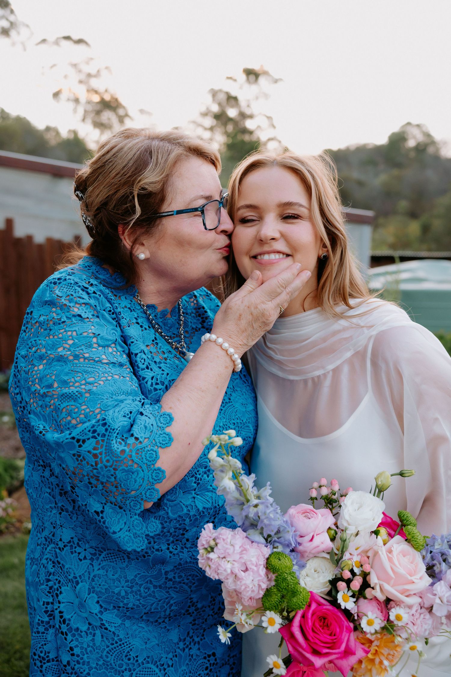 Two people share an intimate moment while holding colorful flower bouquets.