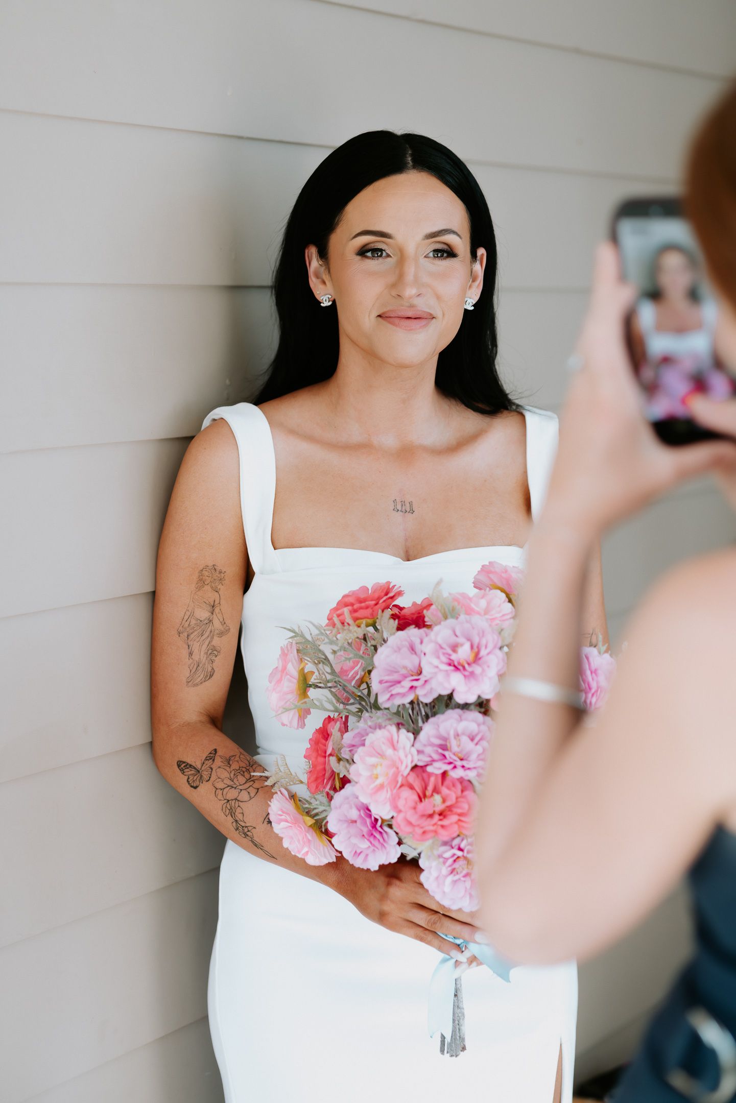 Someone in a white dress holds a beautiful bouquet of pink carnations and roses while having their photo taken.