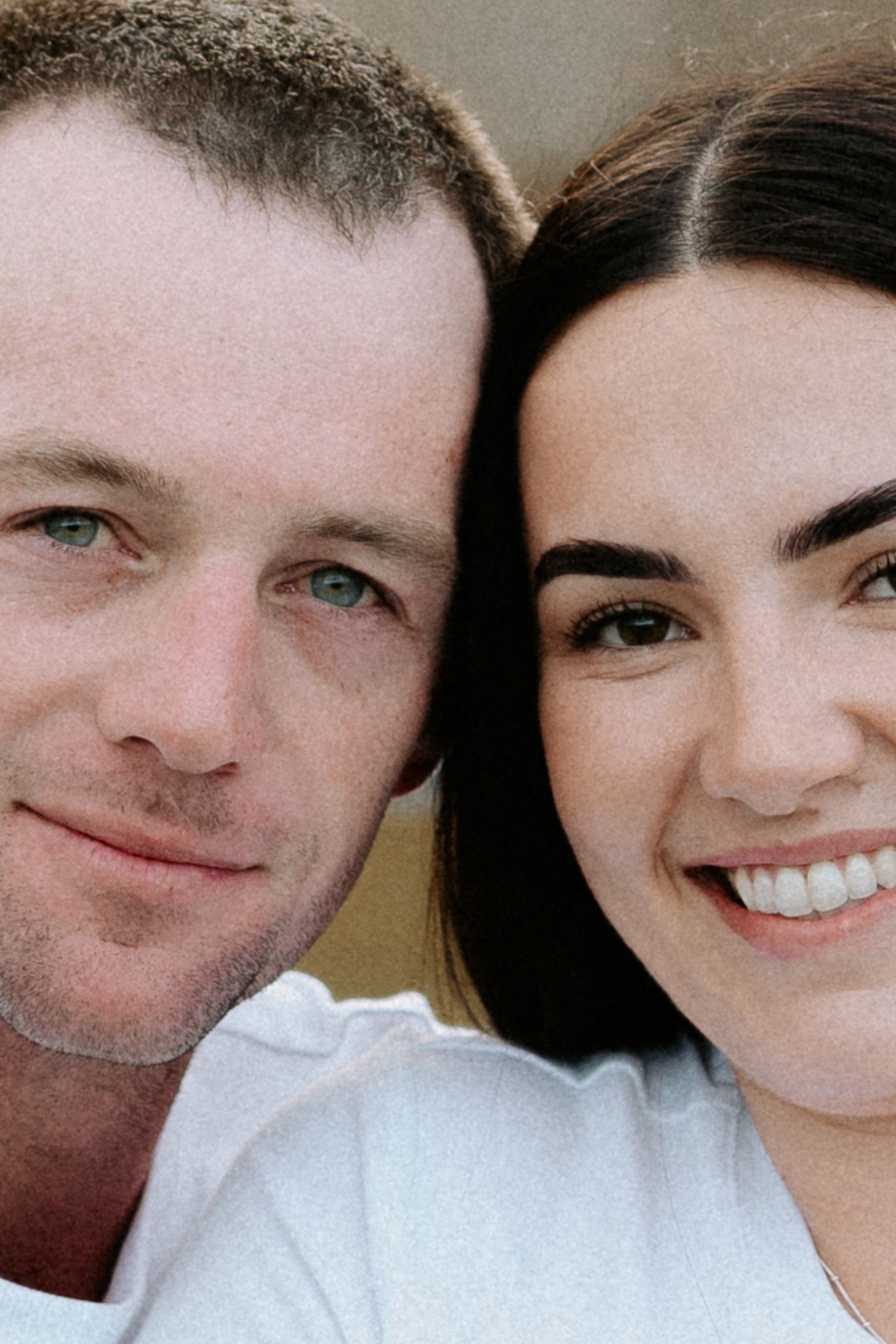 Close-up portrait of a smiling couple, man with blue eyes and woman with dark hair, wearing white shirts.