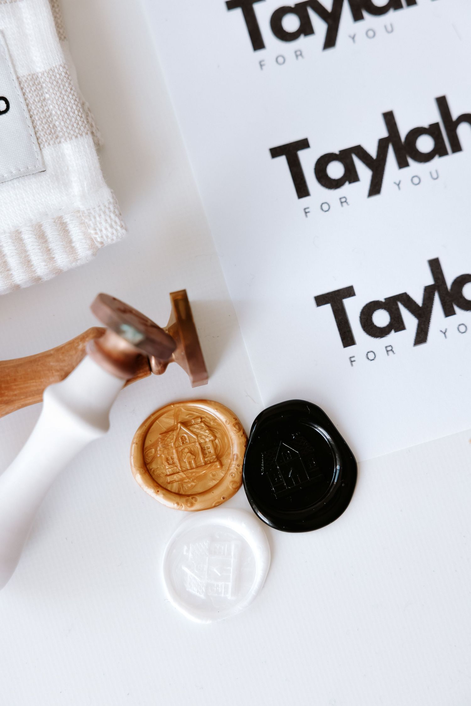 Wax seal stamps with gold, black, and white seals beside Taylah For You branded stationery on white surface.