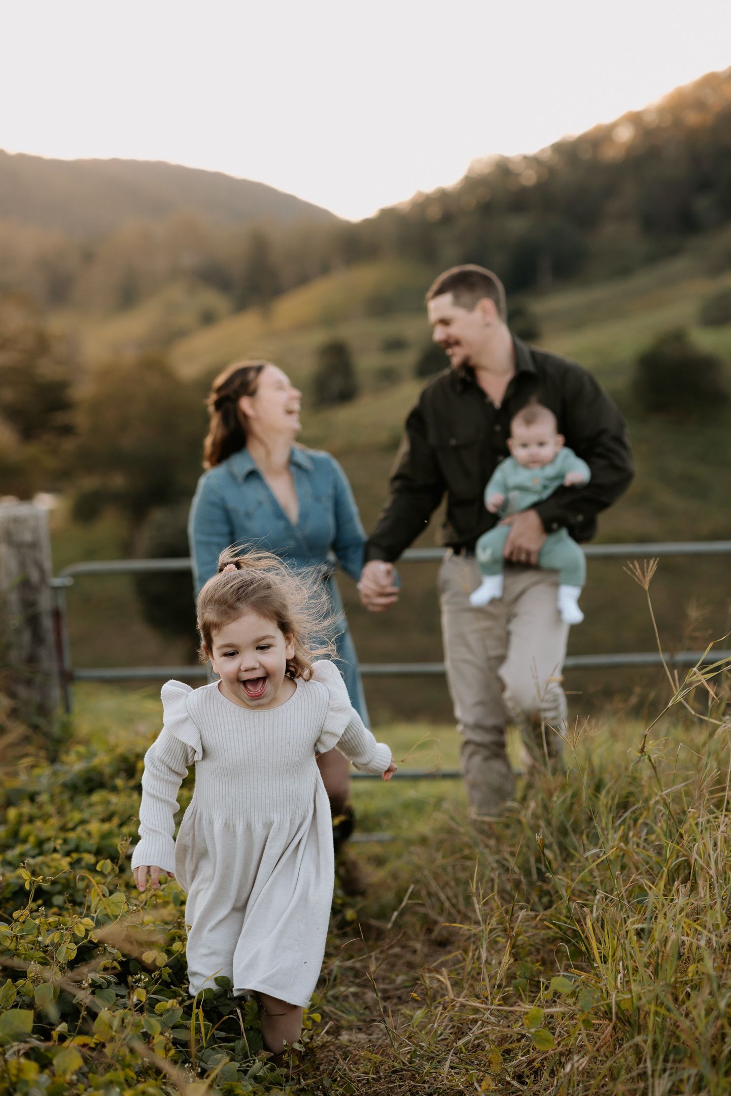A joyful family plays together in a grassy hillside field at golden hour.