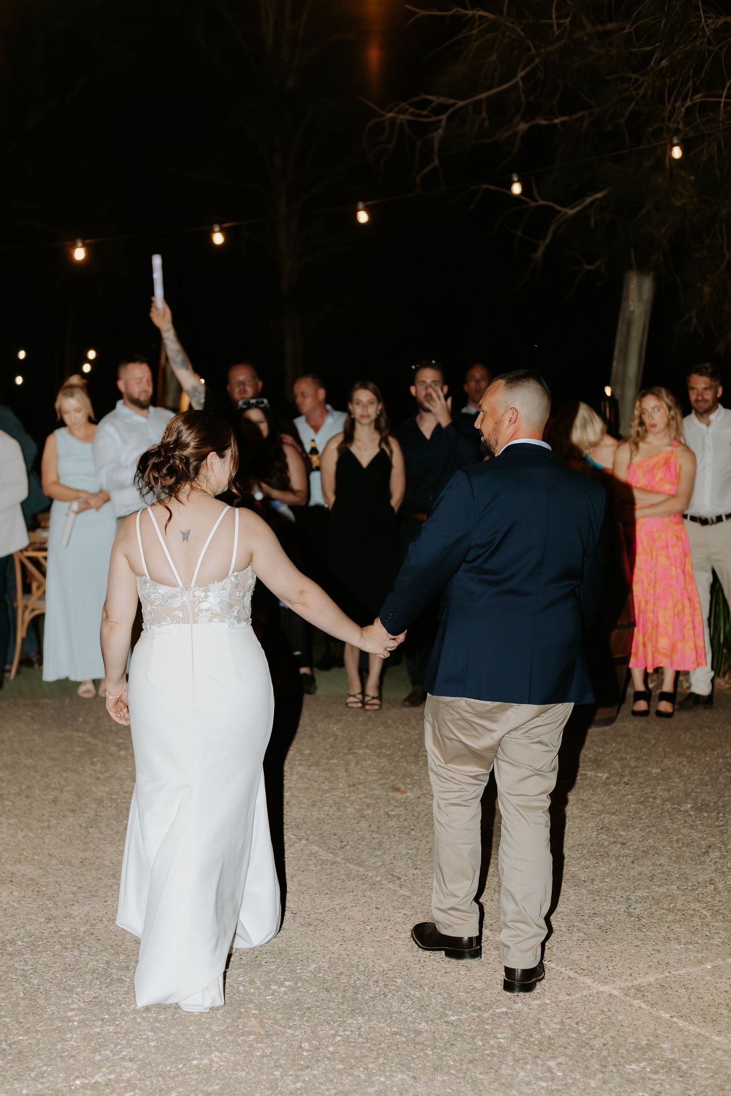 Couple dancing together at nighttime wedding reception with string lights overhead.