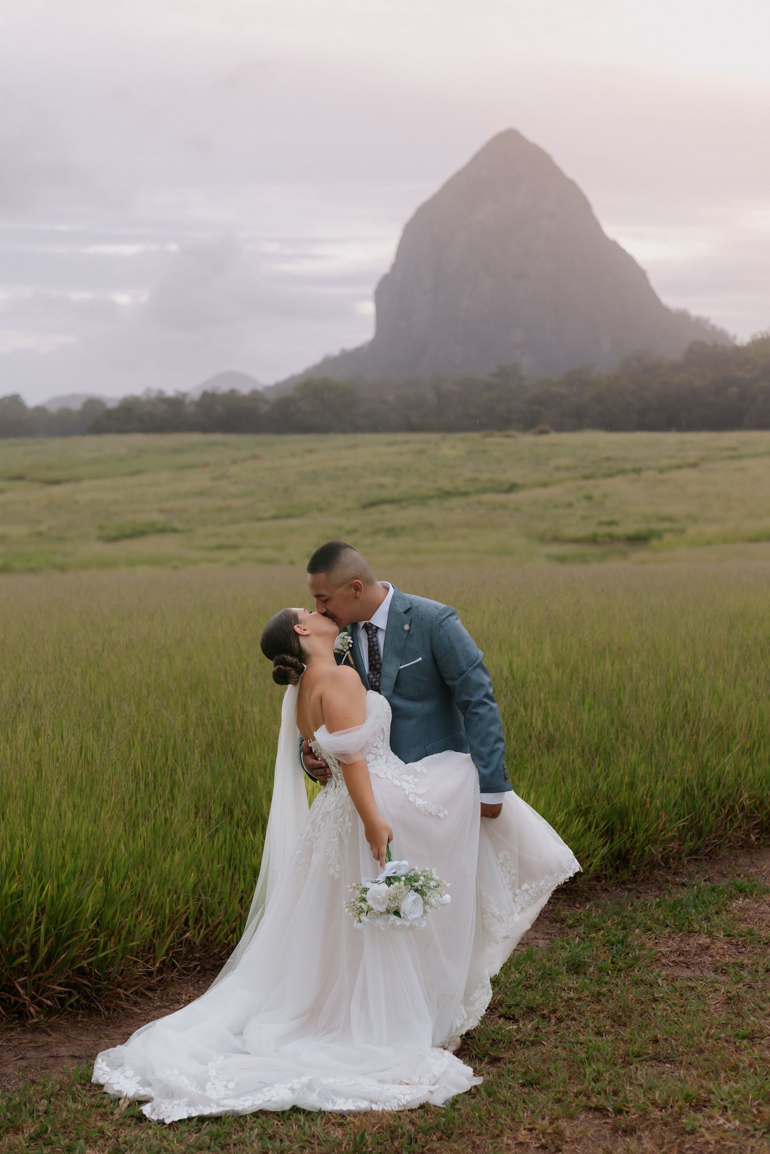 Wedding couple poses in front of a dramatic mountain landscape with flowing white dress.