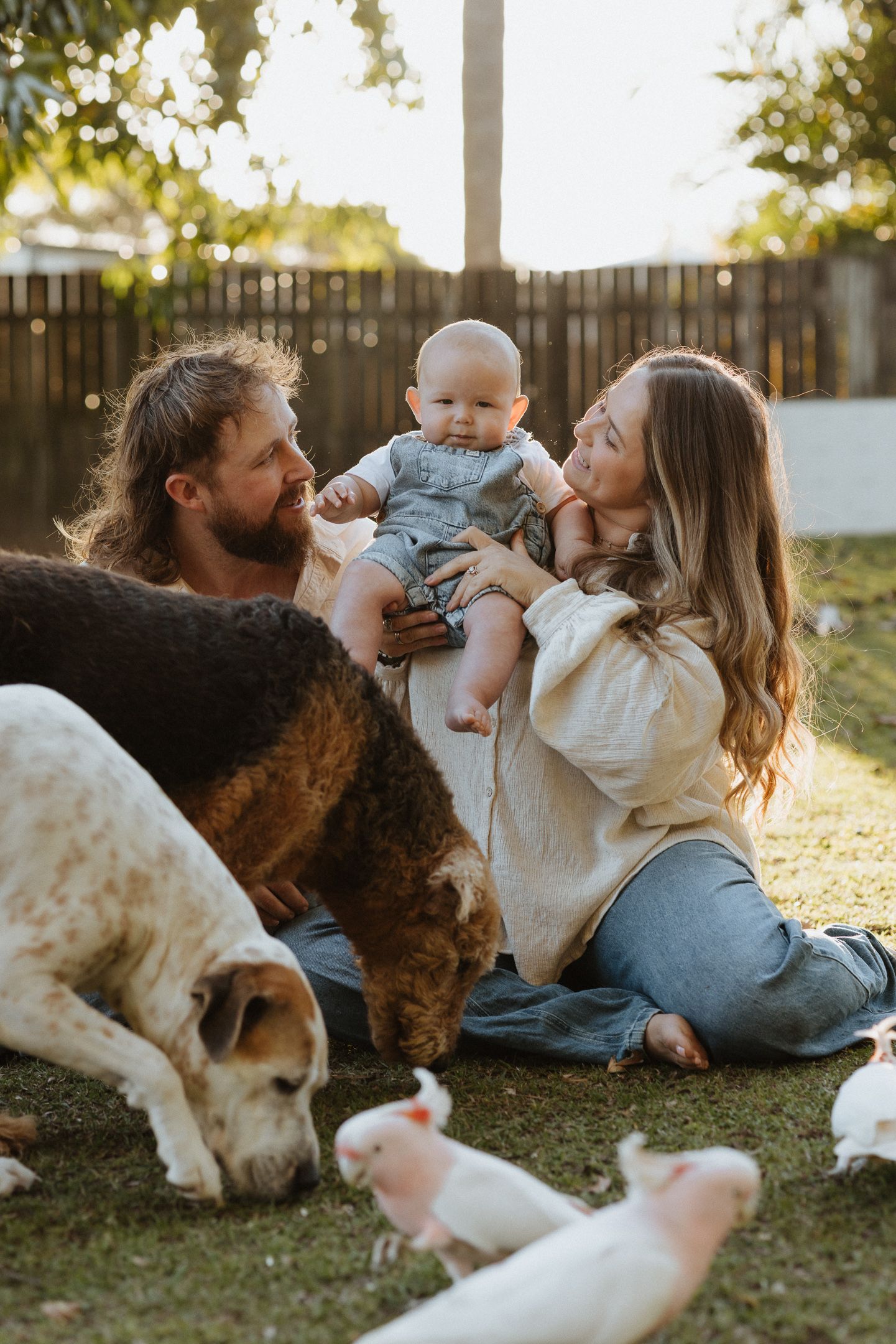 A family and their dog share a tender moment while relaxing together on grass during golden hour.