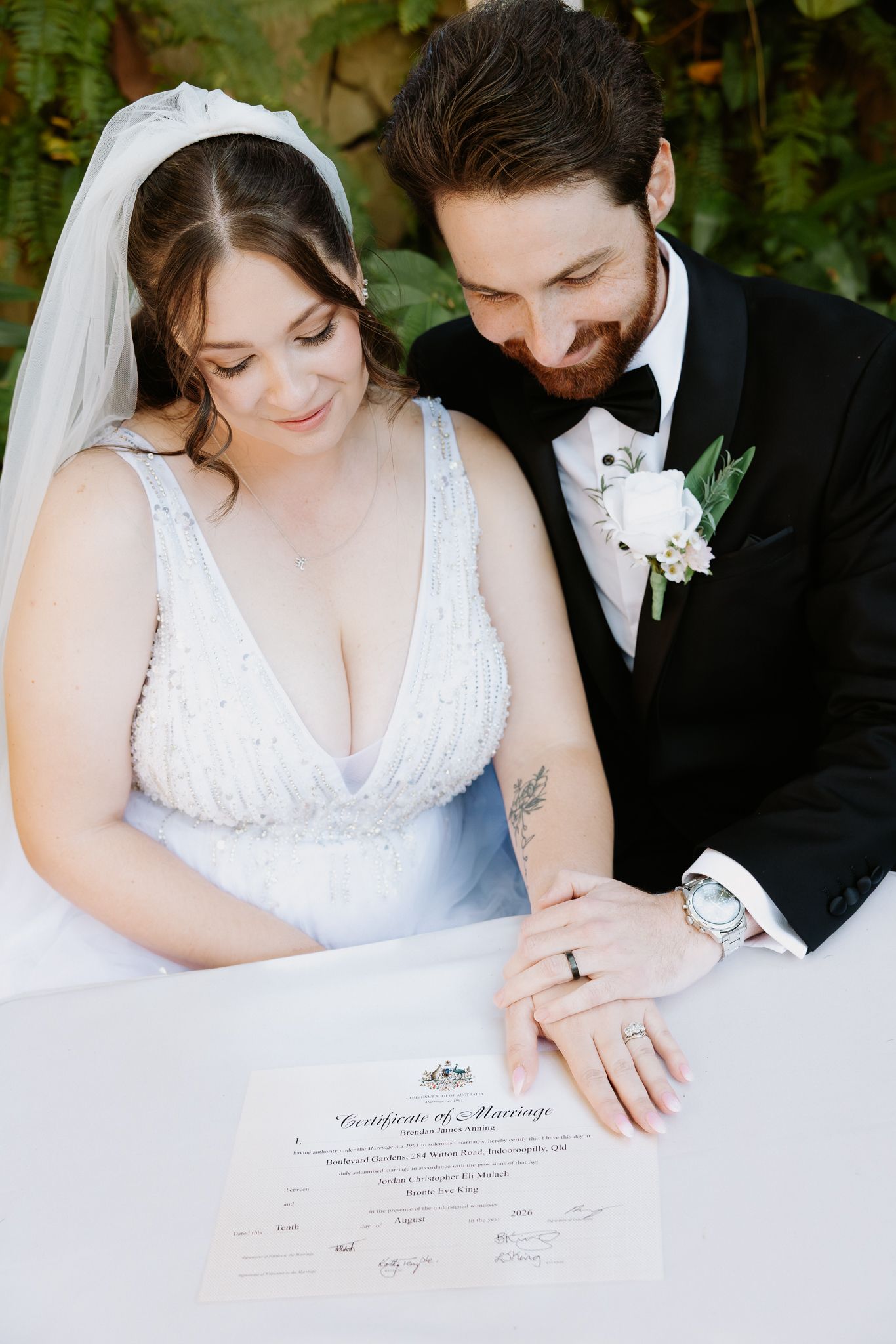 Bride and groom signing their Certificate of Marriage, wearing wedding attire with rings visible.