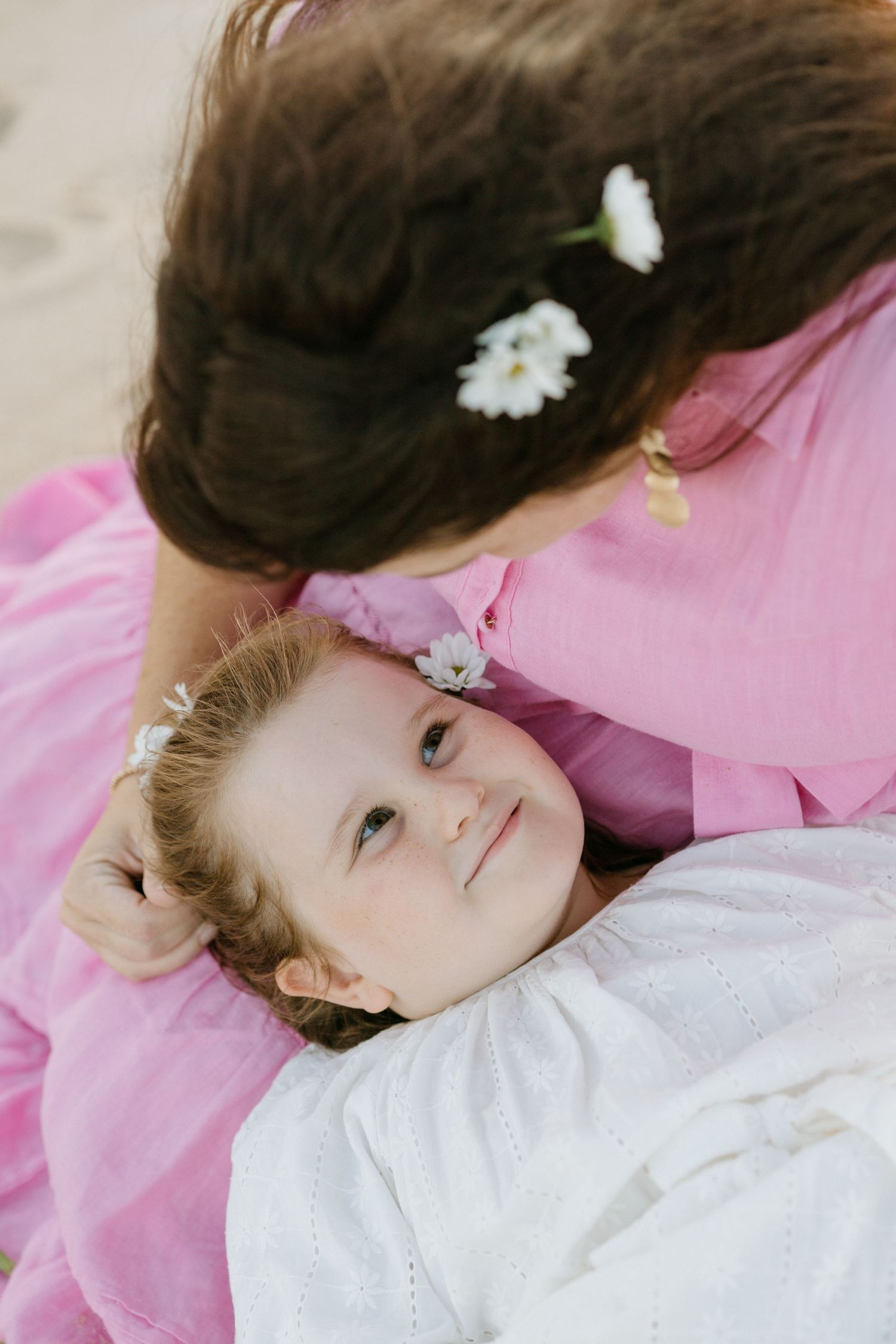 A person in a white dress lying on pink bedding with small white flowers scattered around them.