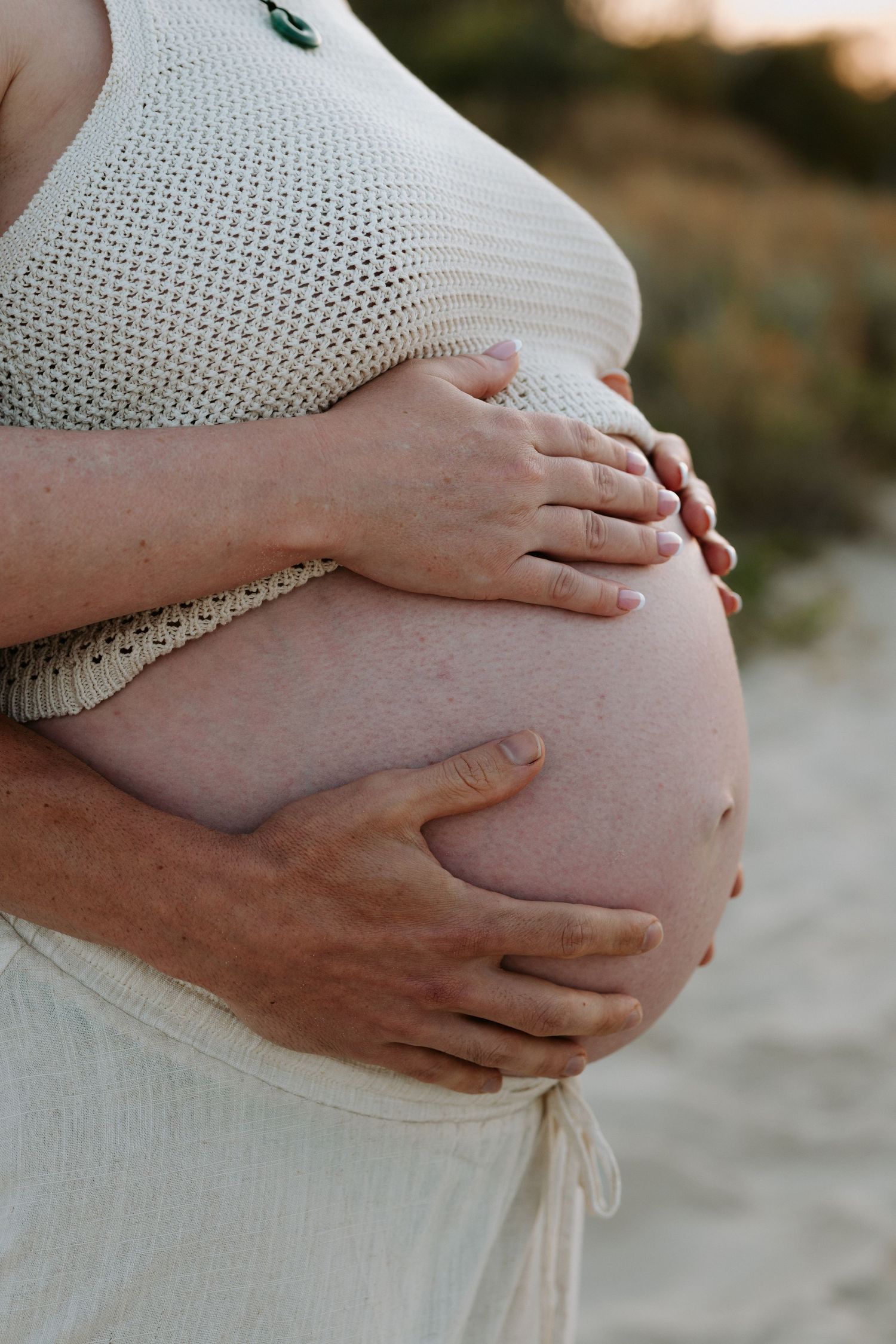 Close-up series of hands gently cradling a pregnant belly in a cream knit sweater against a soft blurred background.