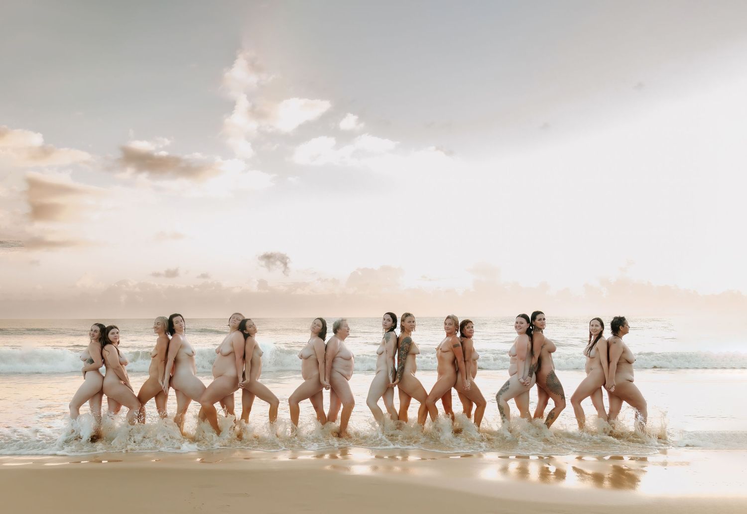 Group of women posing together on a sandy beach at sunset with ocean waves in the background.