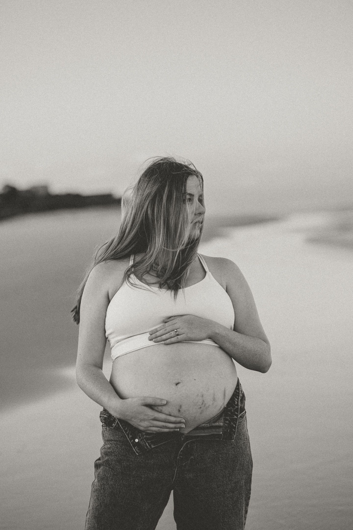 A black and white photo series showing a pregnant belly in jeans with hands cradling it from different angles.