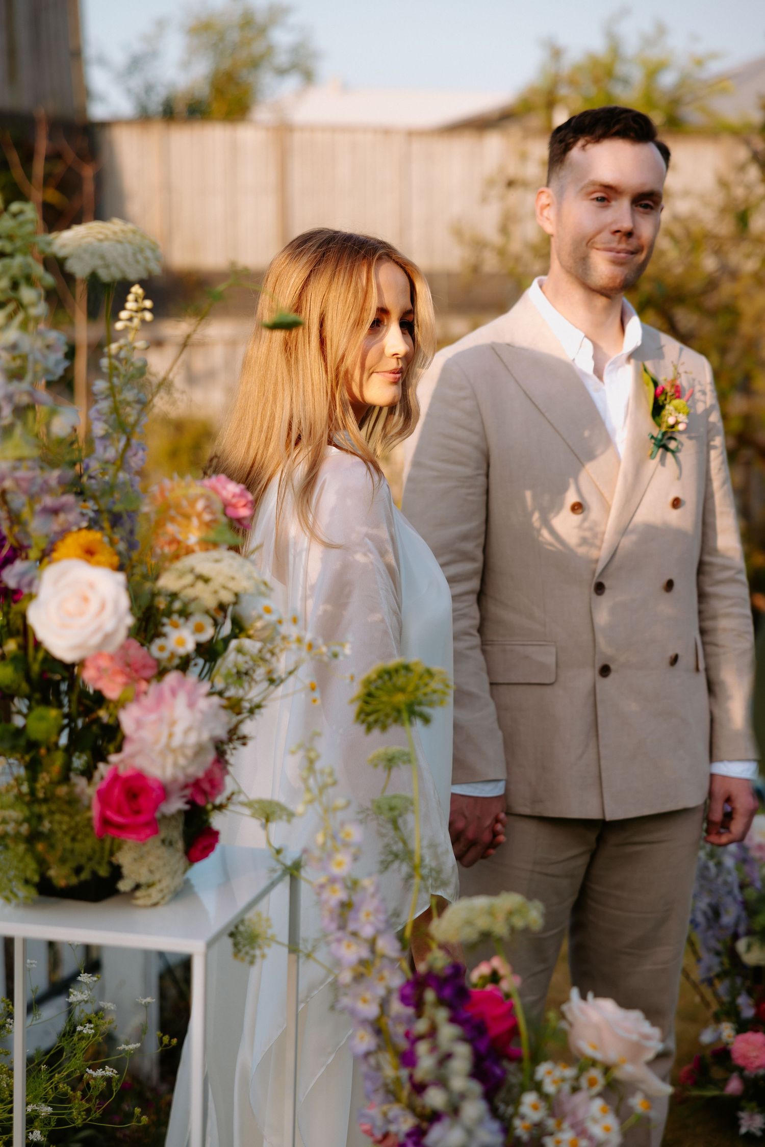 A couple poses in a garden setting with beautiful floral arrangements.