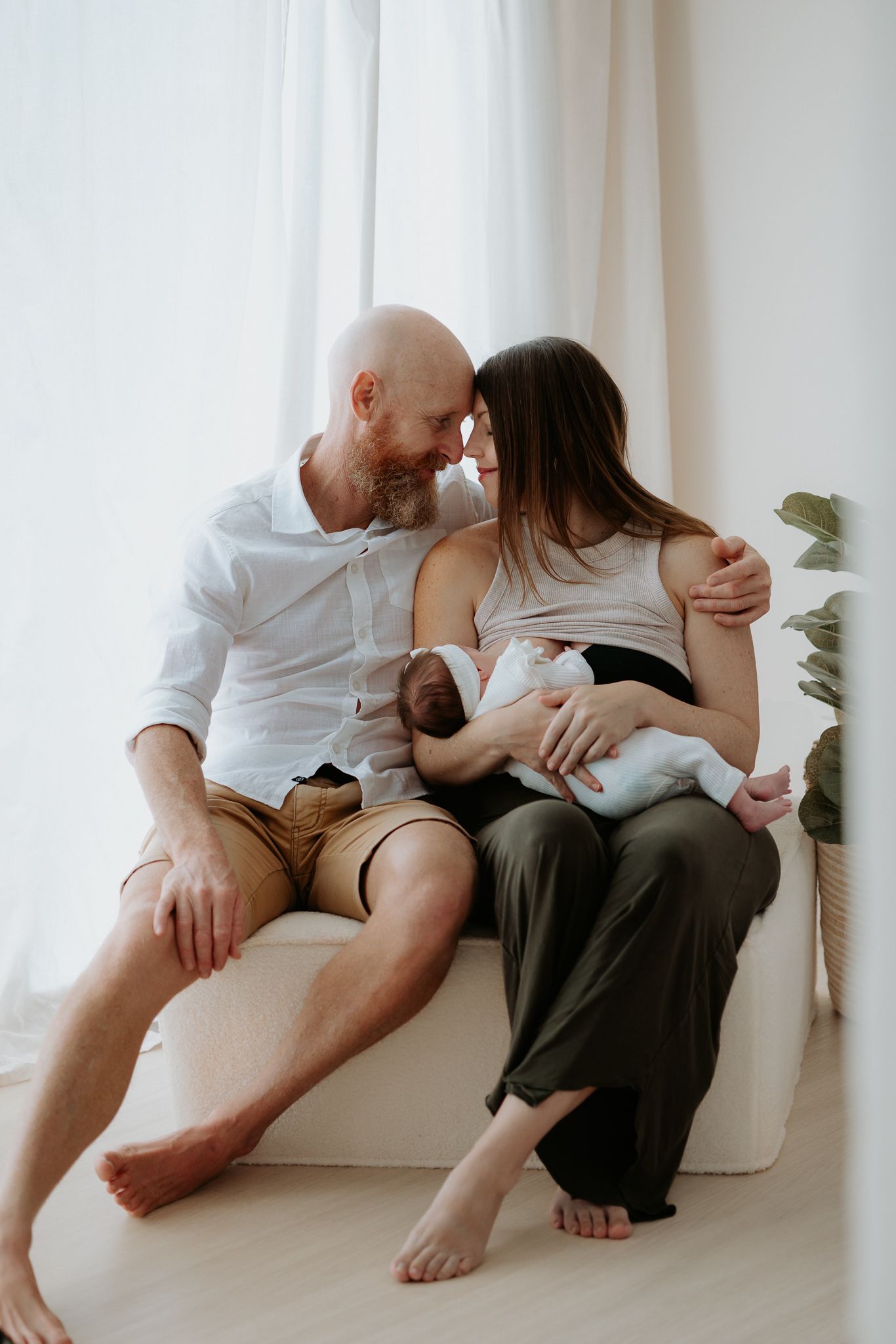 Intimate couple in white and dark clothing sitting together on floor against white wall in minimalist setting.
