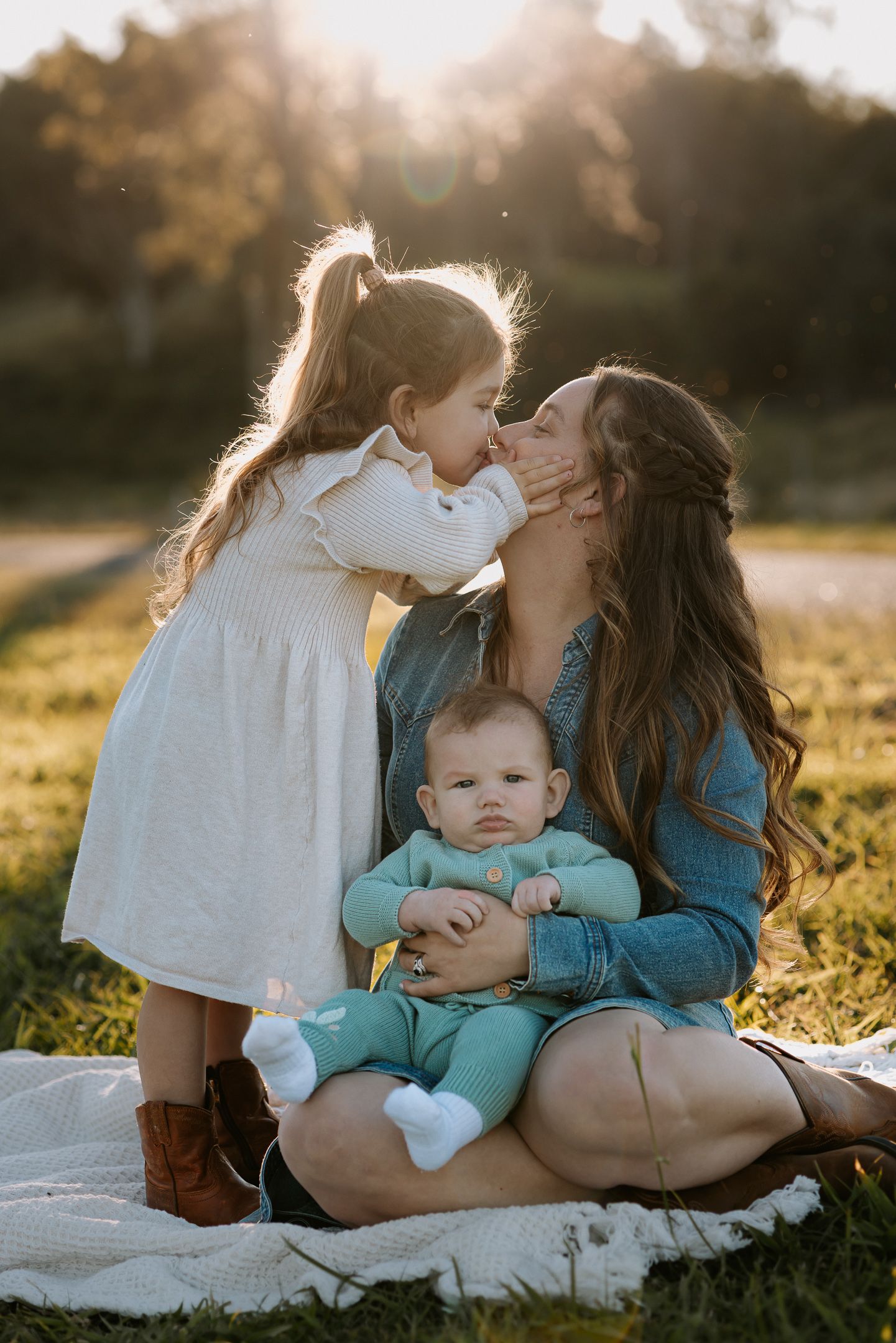 Family sitting together on blanket in grass during golden hour sunset with beautiful backlit glow.