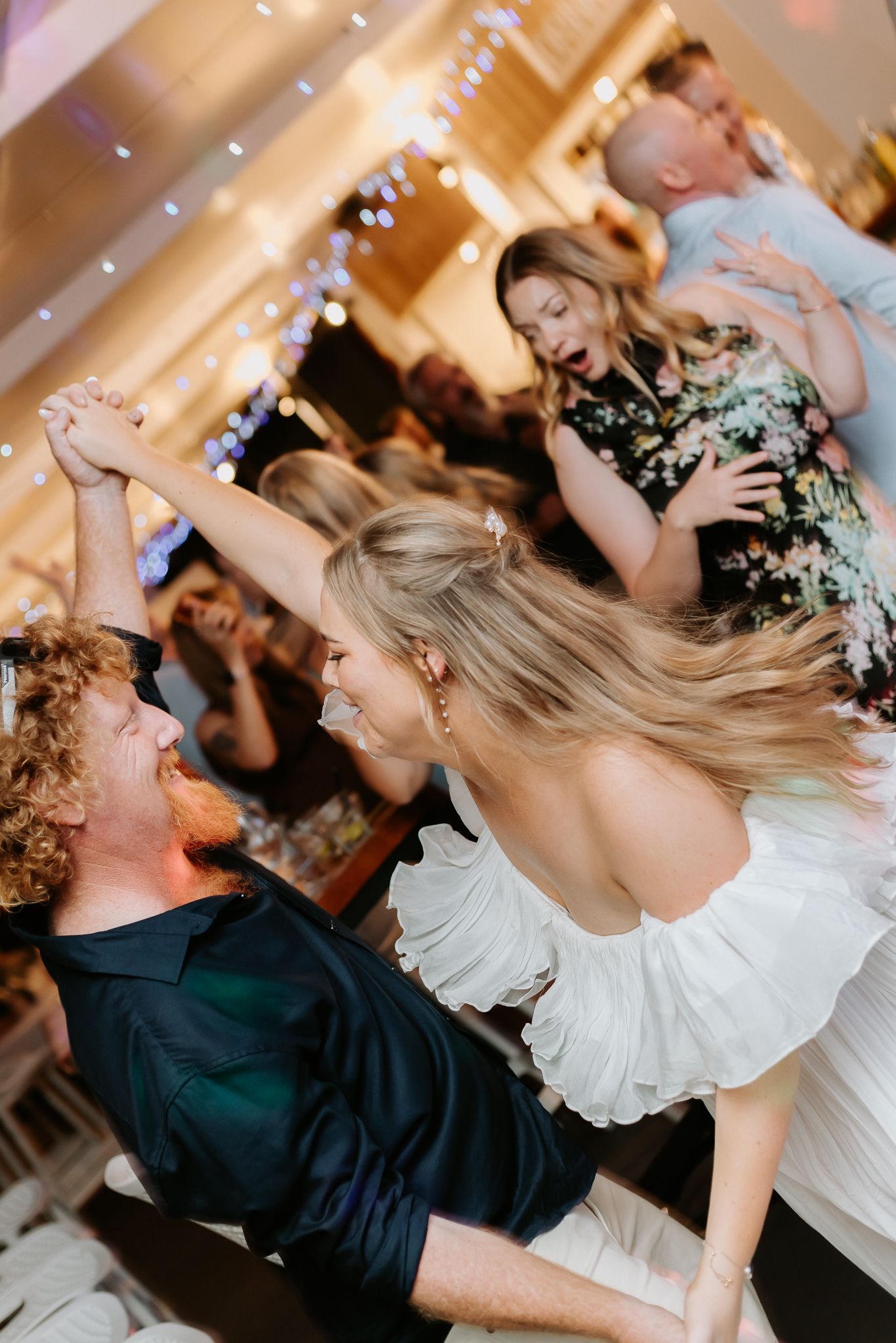 Bride in white dress dancing energetically with guests at a lively wedding reception party.