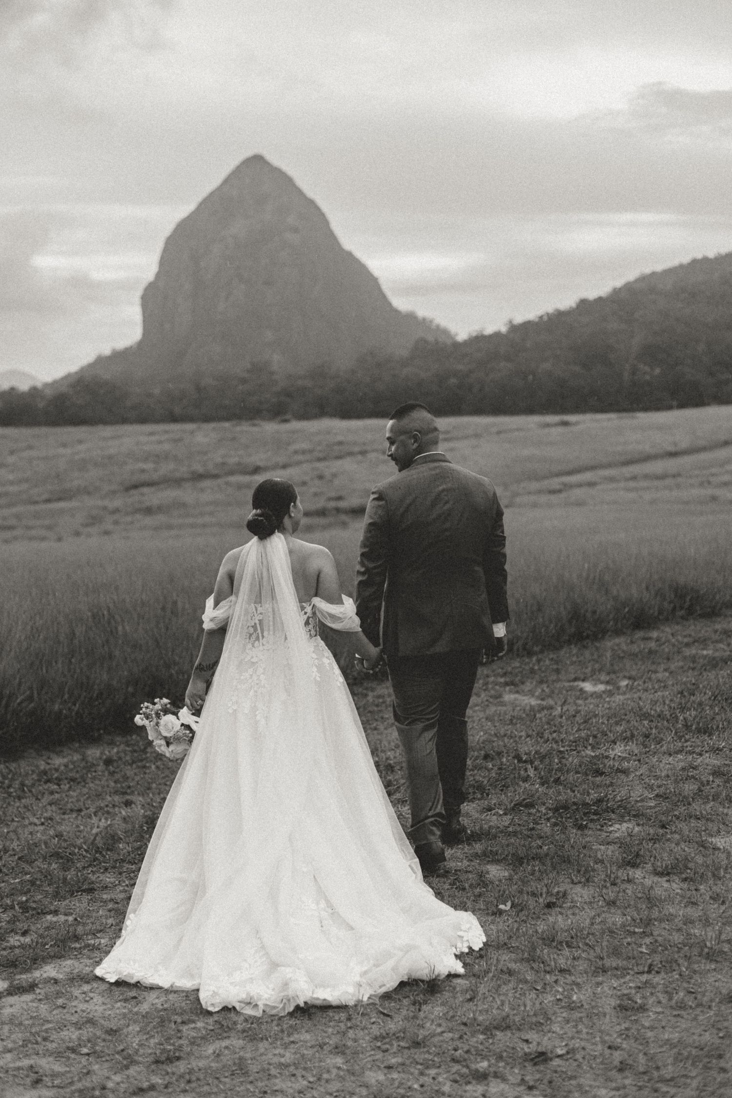 Newlyweds walk through scenic mountain landscape with flowing white wedding dress and veil.