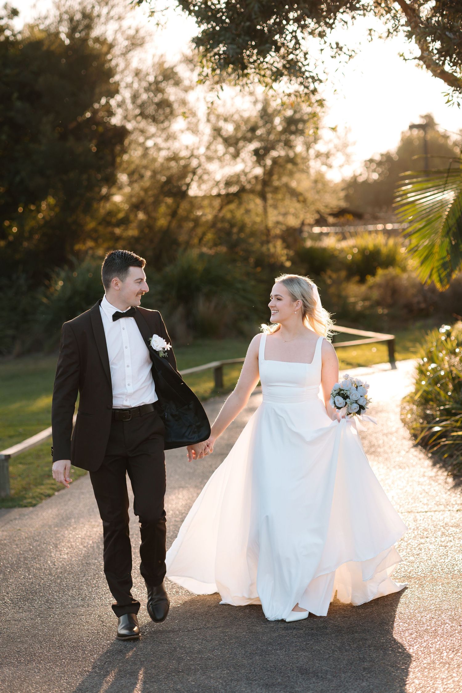 A couple walking together on a path during golden hour in formal wedding attire.