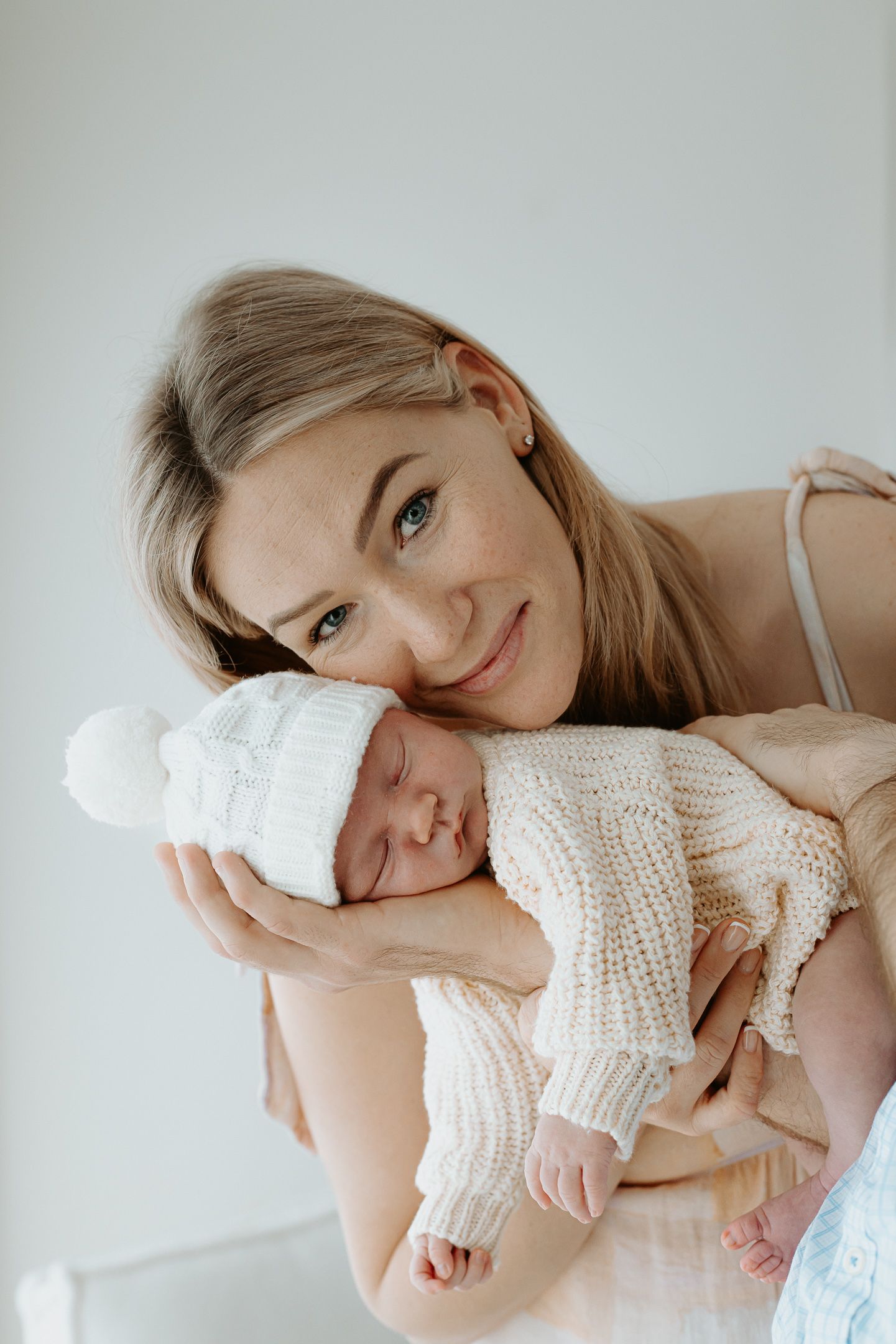 A tender moment between parent and newborn baby wearing soft knit clothing against a light background.