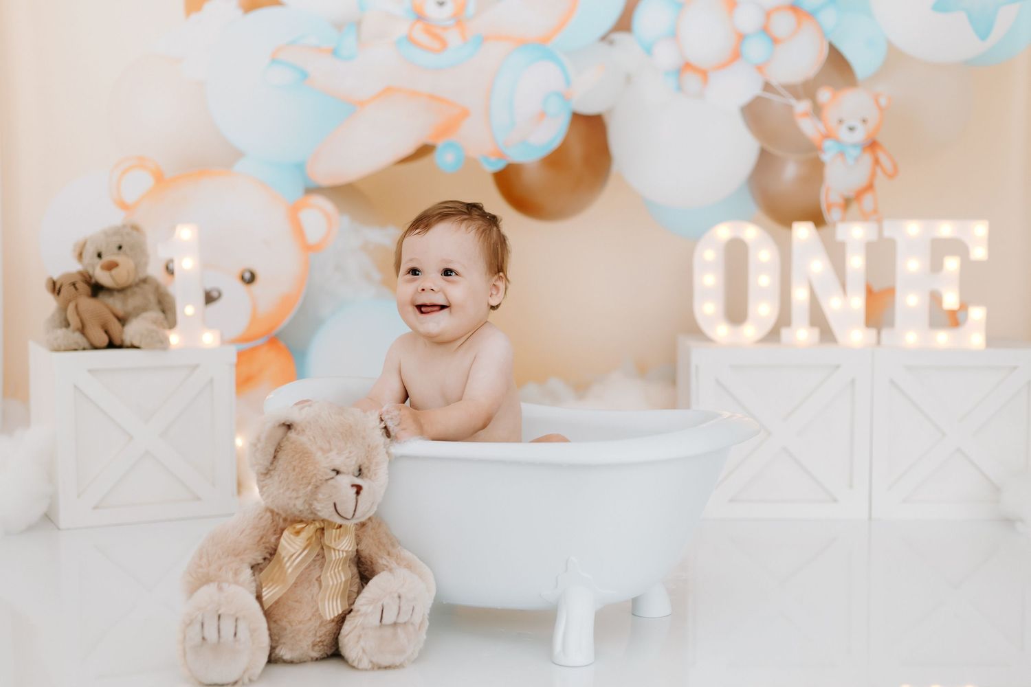 A collection of baby's first birthday photos with pastel blue and white decorations and a teddy bear theme.